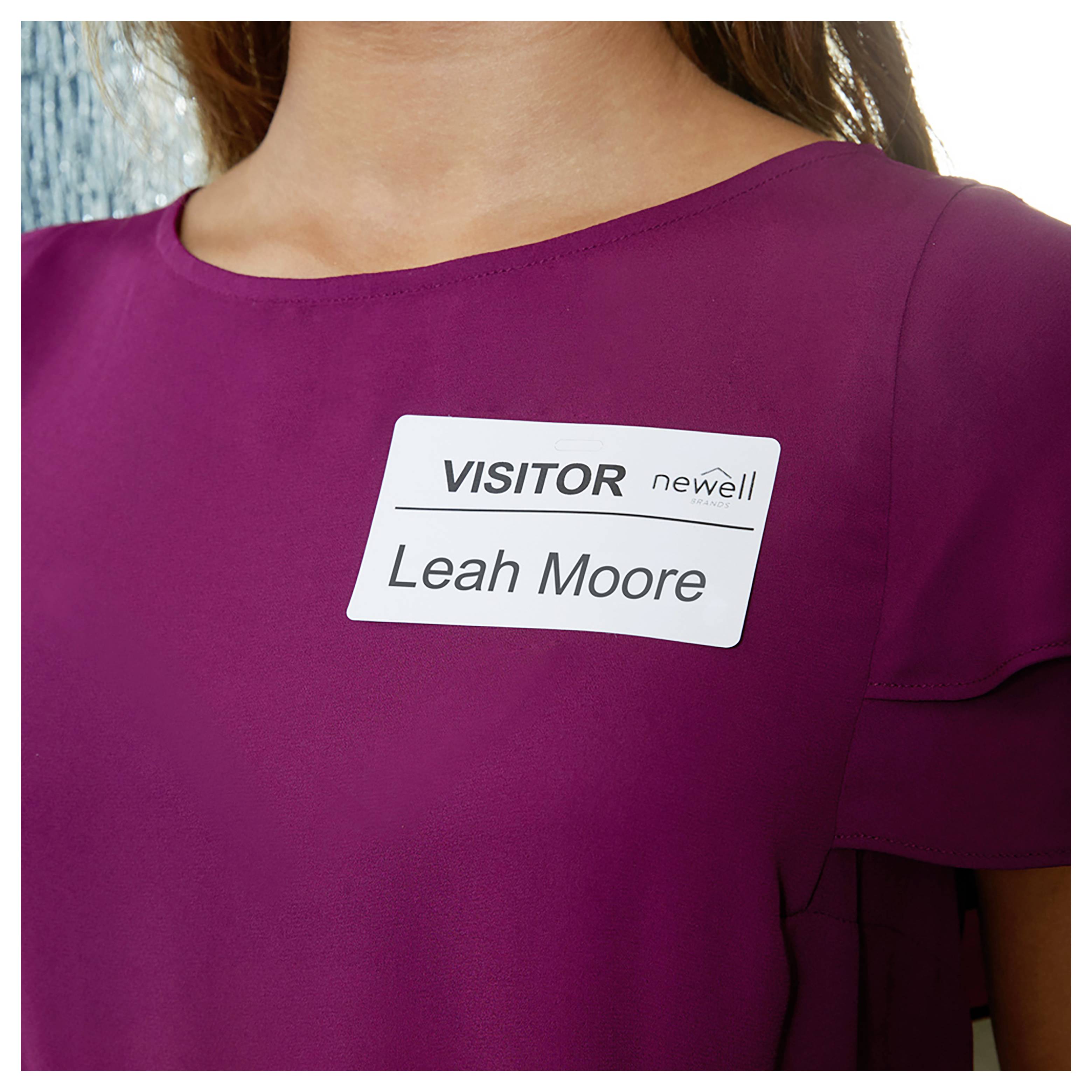 Un badge per visitatore sulla maglietta fucsia di una donna recita "VISITOR" e "Leah Moore" con un piccolo logo "newell".
