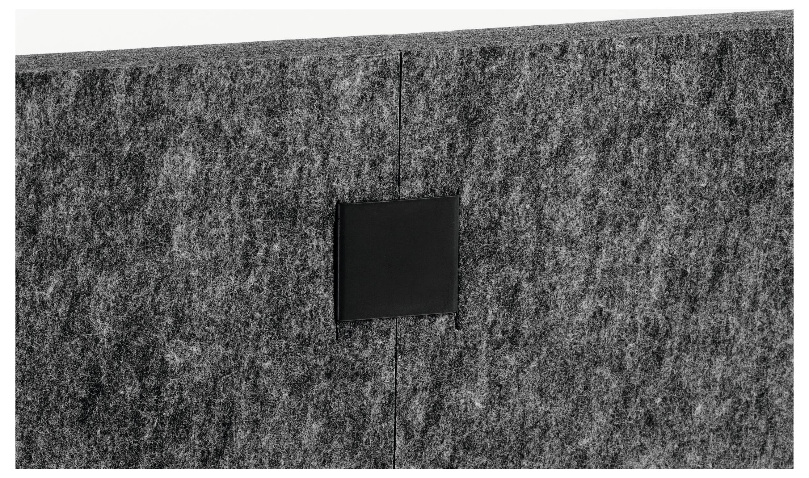Piccolo pannello quadrato nero montato su una parete in feltro grigio o tessuto, centrato su una cucitura verticale.