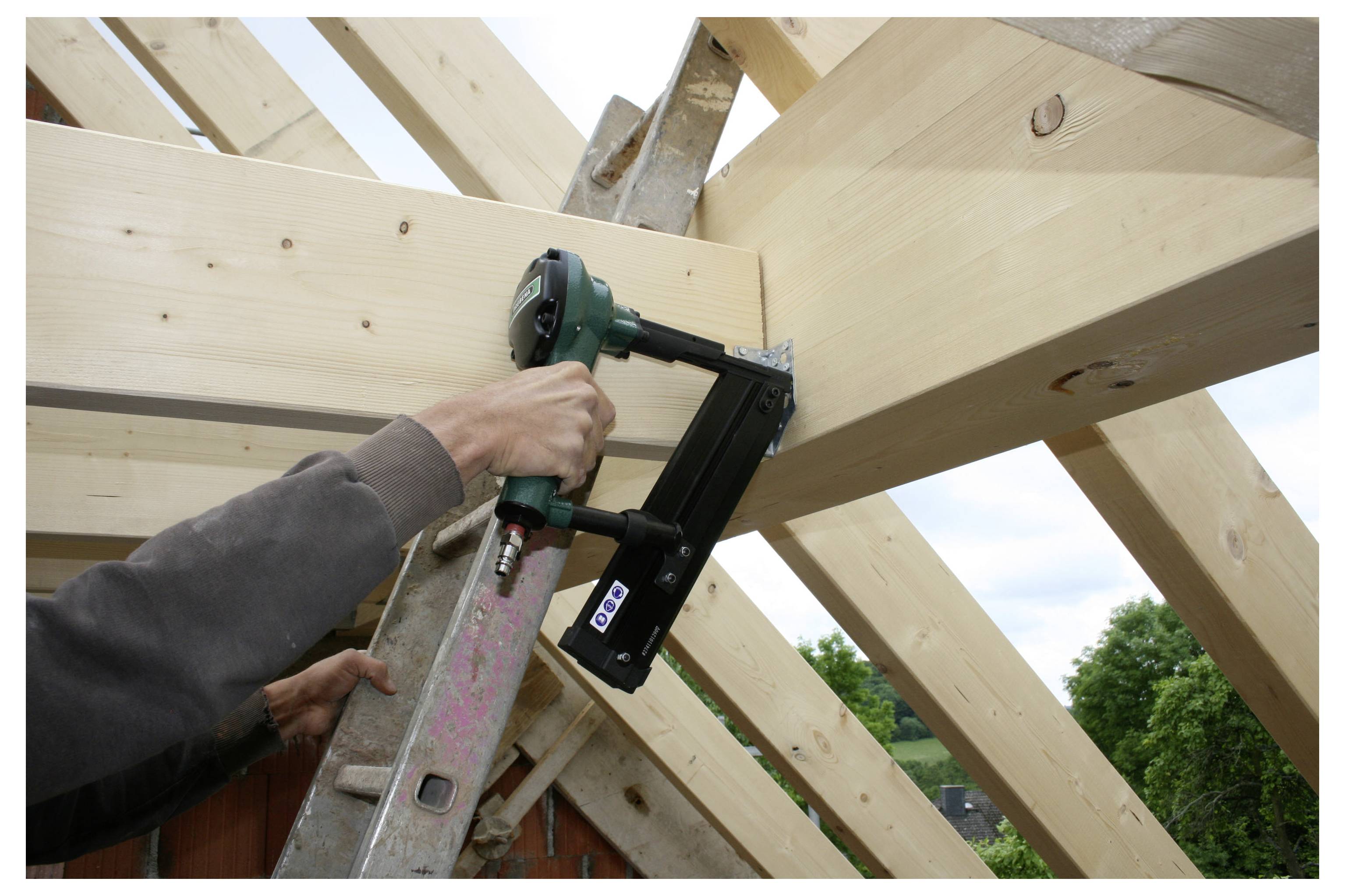 Operaio che utilizza una pistola chiodatrice per fissare le travi di legno del tetto durante la costruzione di una casa.