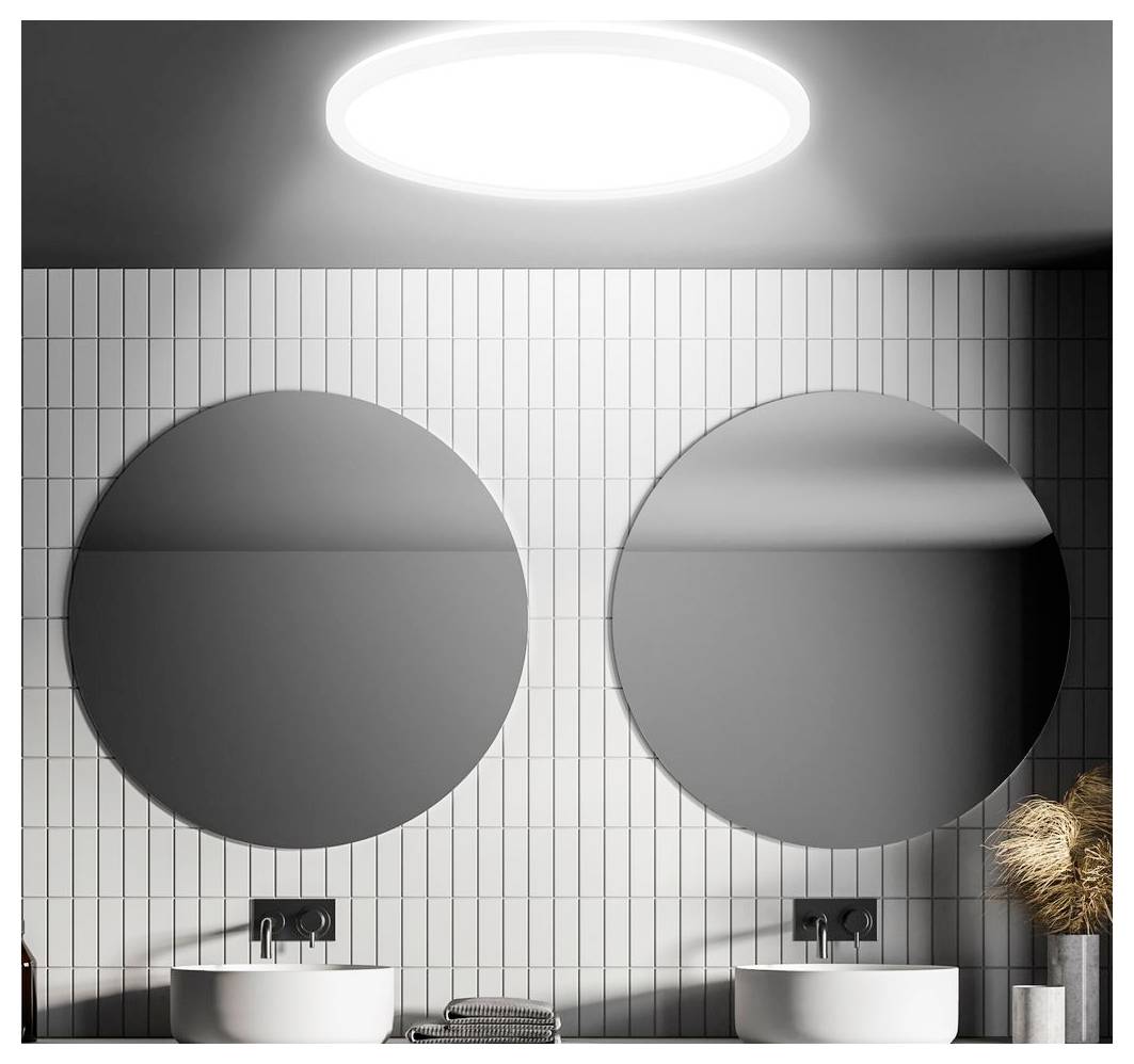 Bagno moderno con due specchi tondi sopra lavabi gemelli a bacile, illuminato da una luce al soffitto e posizionato contro pareti rivestite di piastrelle bianche.