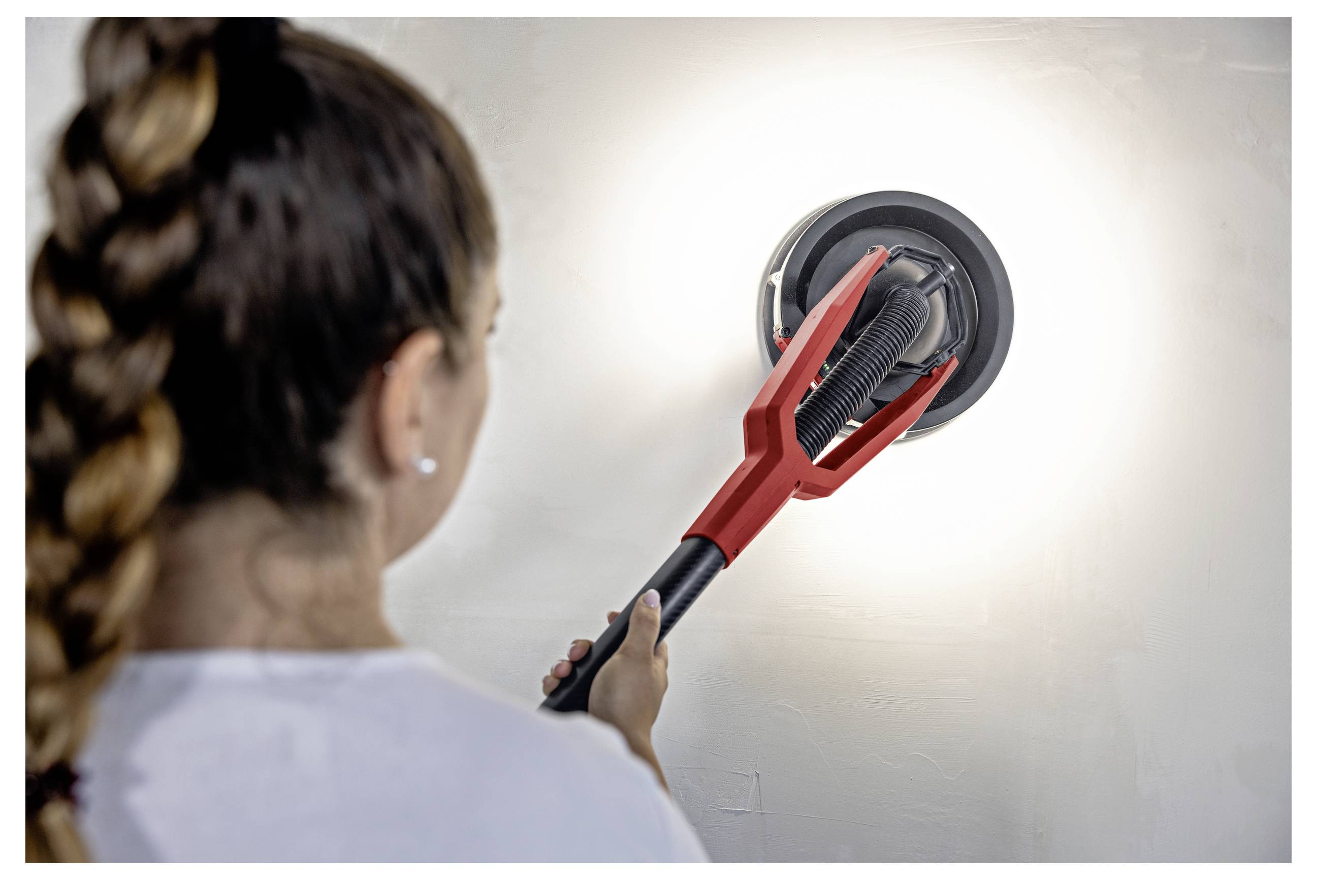 Persona che utilizza una spazzola telescopica rossa per pulire una plafoniera tonda a soffitto o parete.