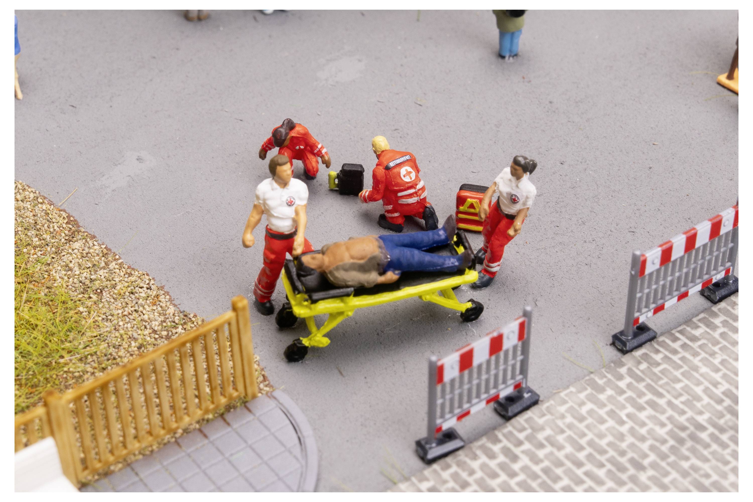 I responsabili dell'emergenza caricano un uomo ferito su una barella accanto alle barriere stradali, suggerendo una scena di incidente.