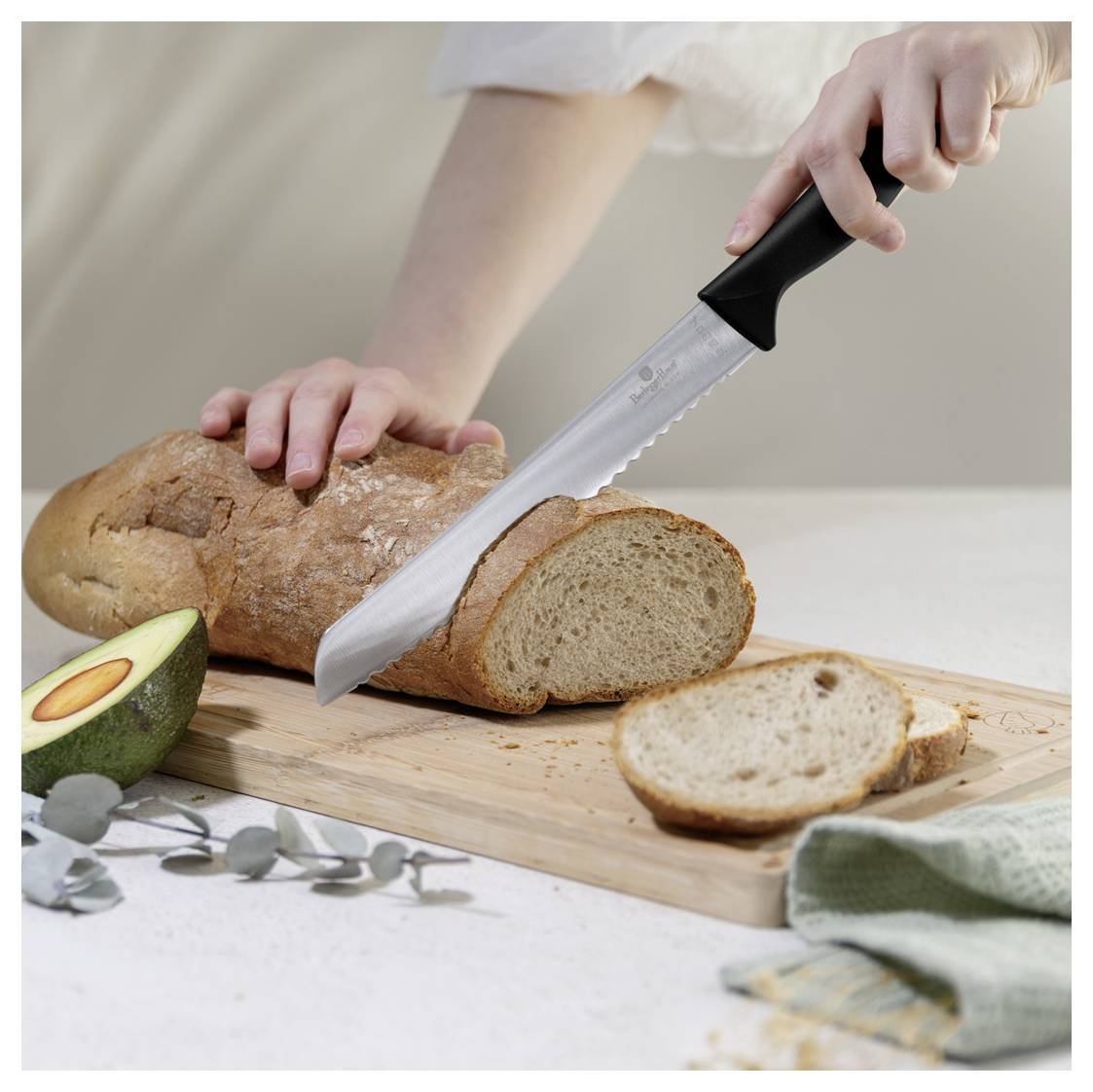 Le mani affettano un pane su un tagliere, con un pezzo già tagliato e un avocado nelle vicinanze.