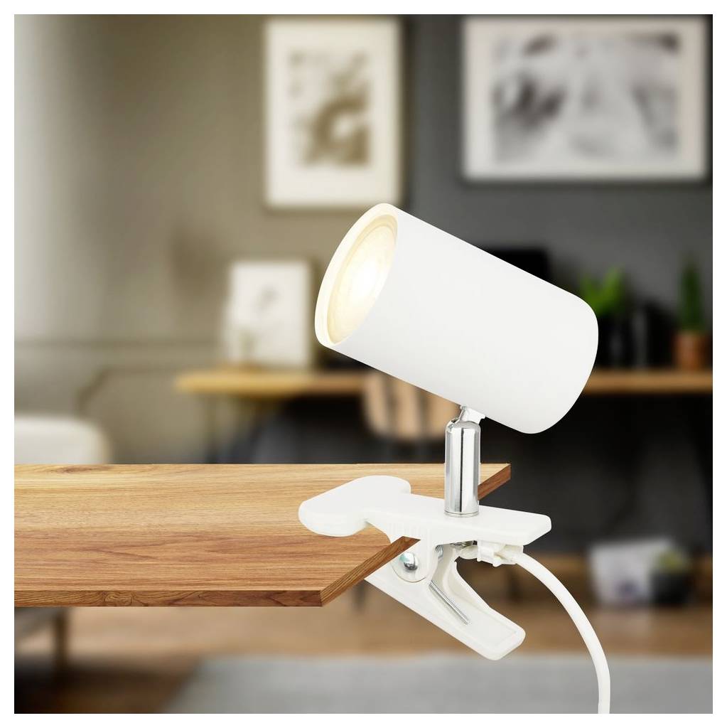 Lampada da scrivania bianca con clip aggancia a un bordo di tavolo in legno in una stanza moderna, con cavo di alimentazione visibile.