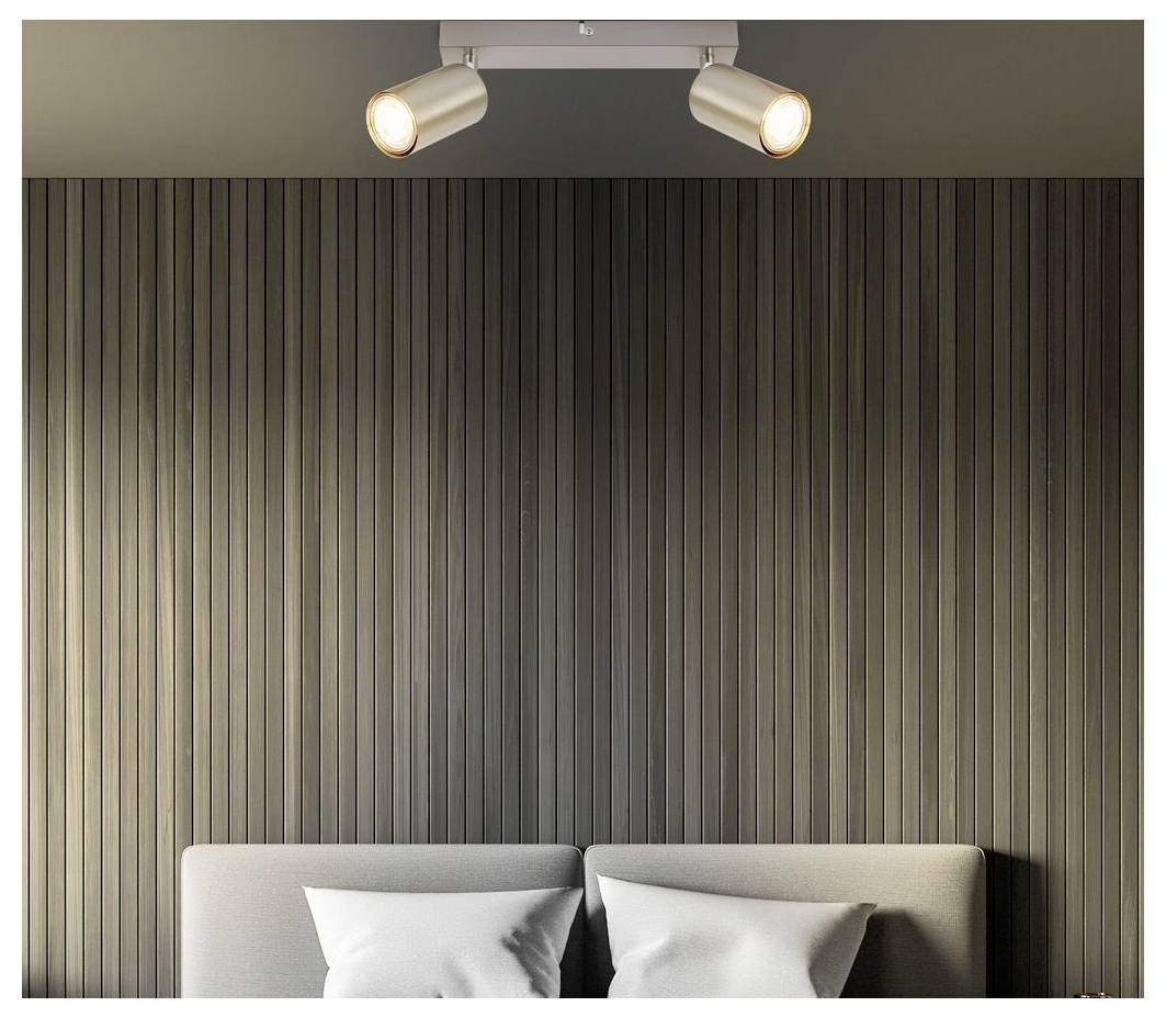 Camera da letto moderna con un letto imbottito grigio e cuscini contro una parete rivestita di doghe verticali scure, illuminata da due faretti a soffitto.
