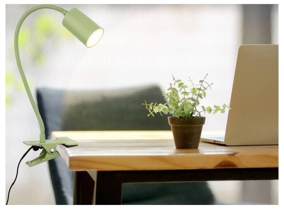 Lampada da scrivania verde con clip illumina un tavolo in legno con una piccola pianta in vaso e laptop aperto in uno spazio di lavoro domestico luminoso.