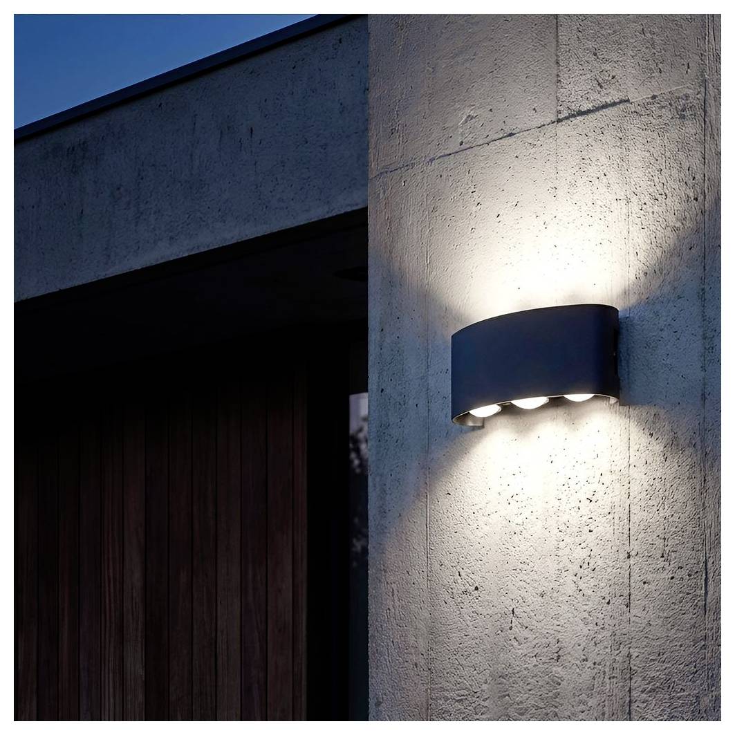 Luce da parete esterna montata su un muro esterno in cemento sopra una porta scura, che proietta un cono di luce brillante.