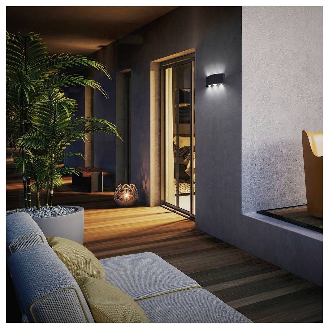 Patio moderno con una sdraio, una palma in vaso, una terrazza in legno caldo, una luce da parete e una porta scorrevole aperta che dà su una stanza interna al tramonto.