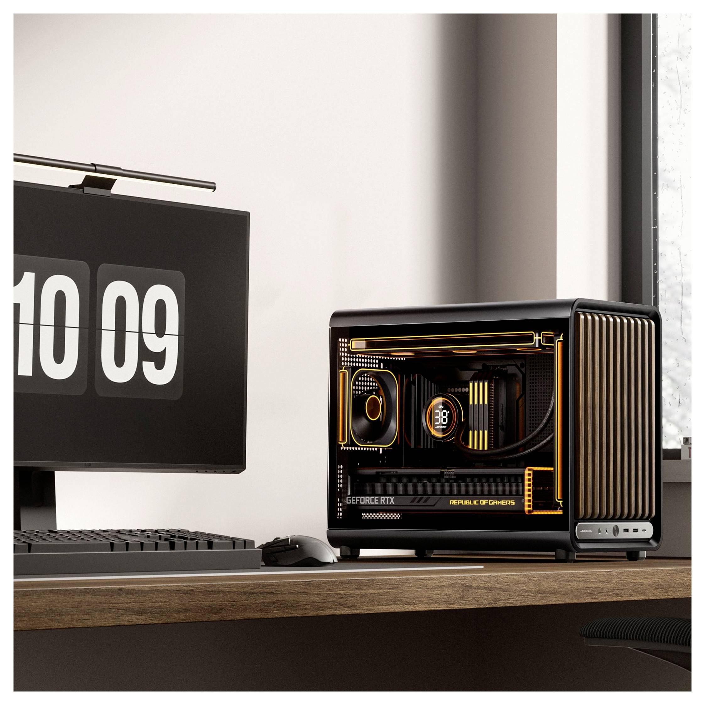 Setup desktop con un monitor che mostra '10 09' accanto a una torre PC gaming compatta e illuminata su una scrivania in legno.