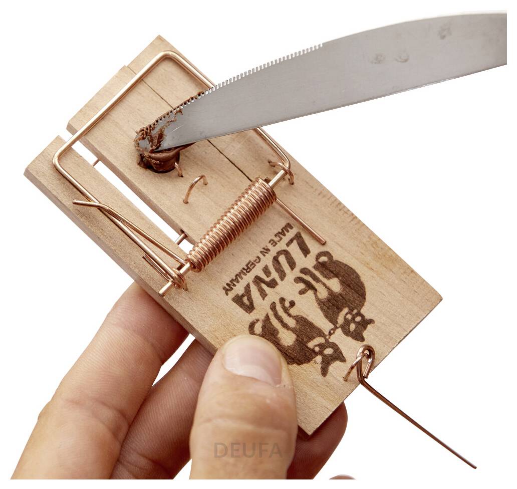 Una mano che tiene una trappola per topi mentre un coltello ne fa scattare il meccanismo, mostrando un'installazione pericolosa su una trappola in legno etichettata 'LUNA'.