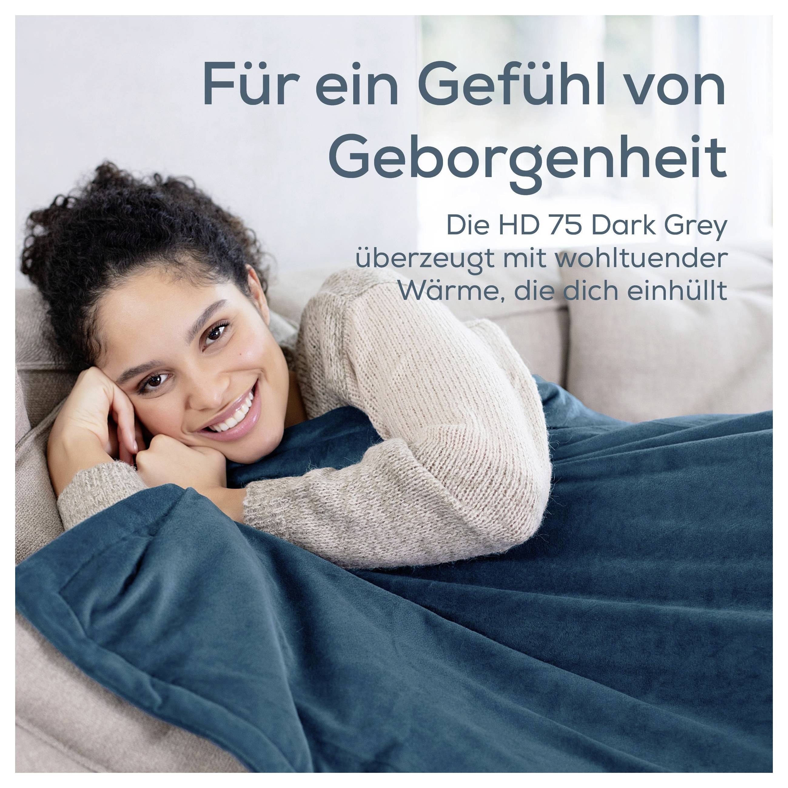 Donna sorridente sdraiata accoccolata sotto una coperta grigio scuro; Testo: 'Per una sensazione di sicurezza' e 'L'HD 75 Dark Grey ... Calore che ti avvolge'.