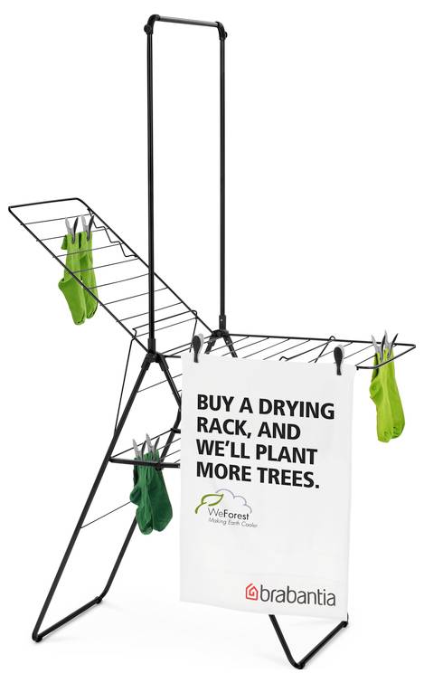 Scaffale per asciugare con bucato e slogan: 'COMPRA UNO SCAFFALE PER ASCIUGARE, E PIANTEREMO PIÙ ALBERI.' Logo di Brabantia e WeForest.