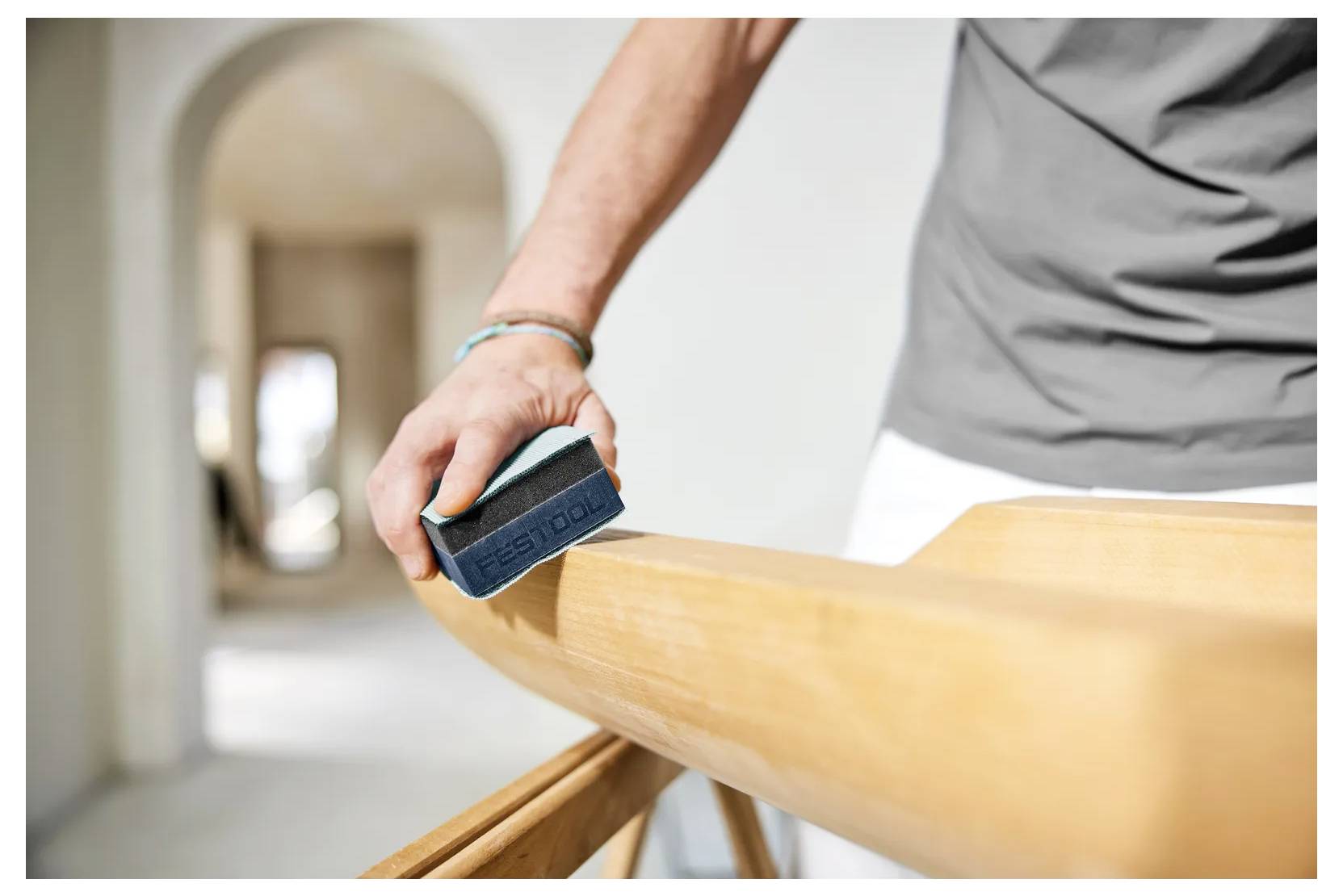 Persona che leviga una ringhiera in legno con un blocco per levigare durante lavori di rifinizione interni.