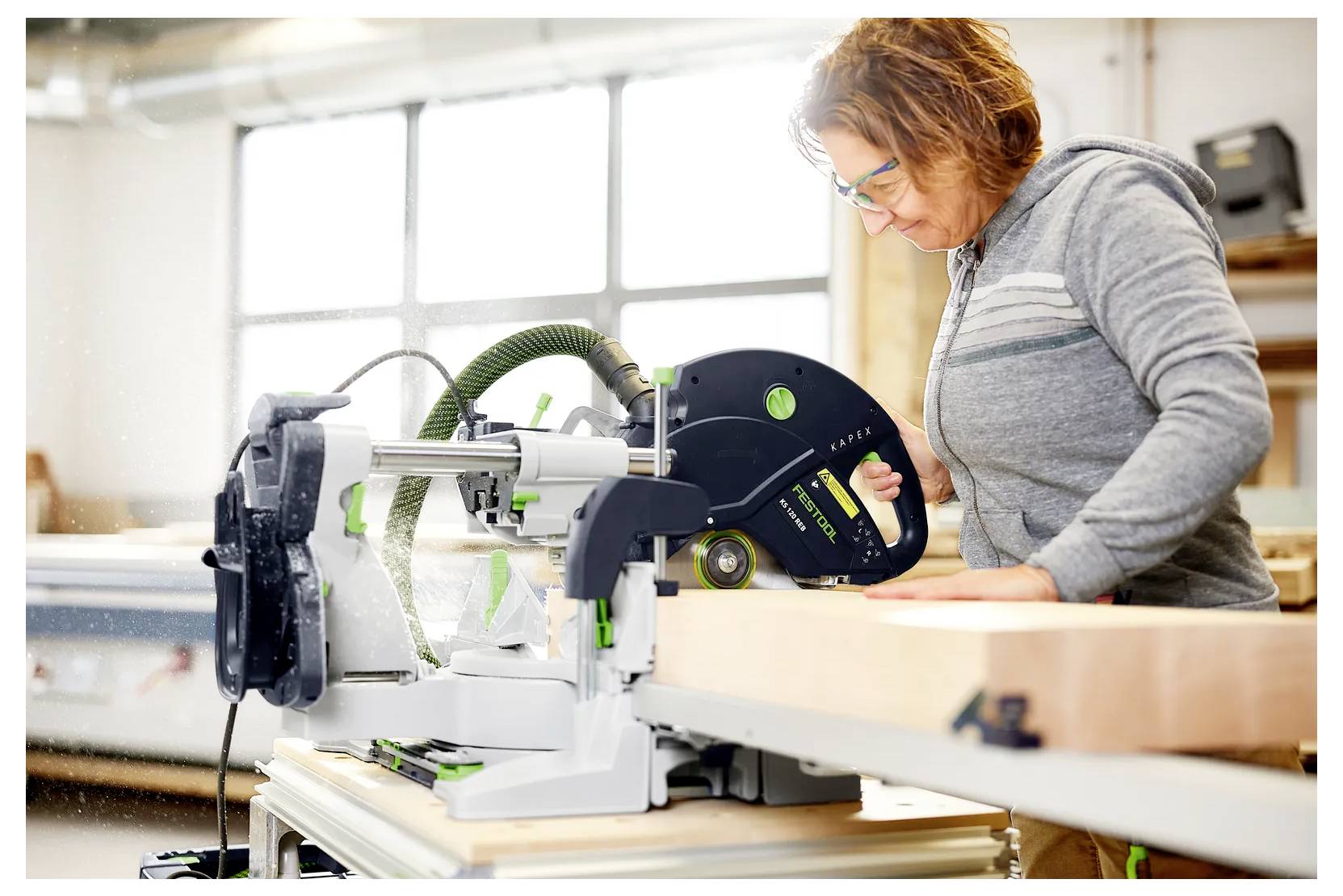 Donna che utilizza una sega circolare per tagliare una lunga tavola di legno in un laboratorio, concentrata sul compito di taglio.