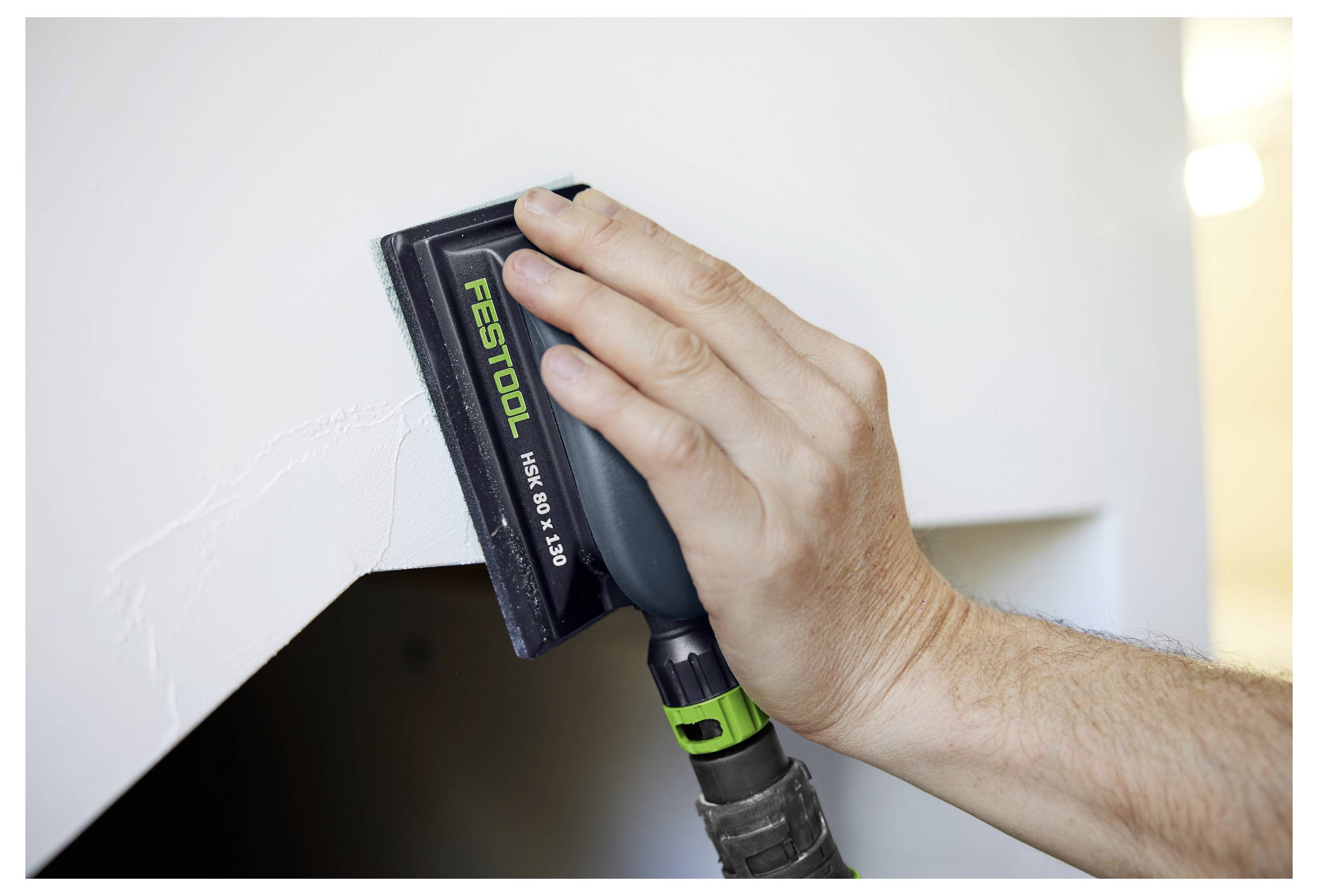 Carteggiatura manuale di un angolo di parete bianca con una levigatrice Festool per levigare una superficie prima della finitura.