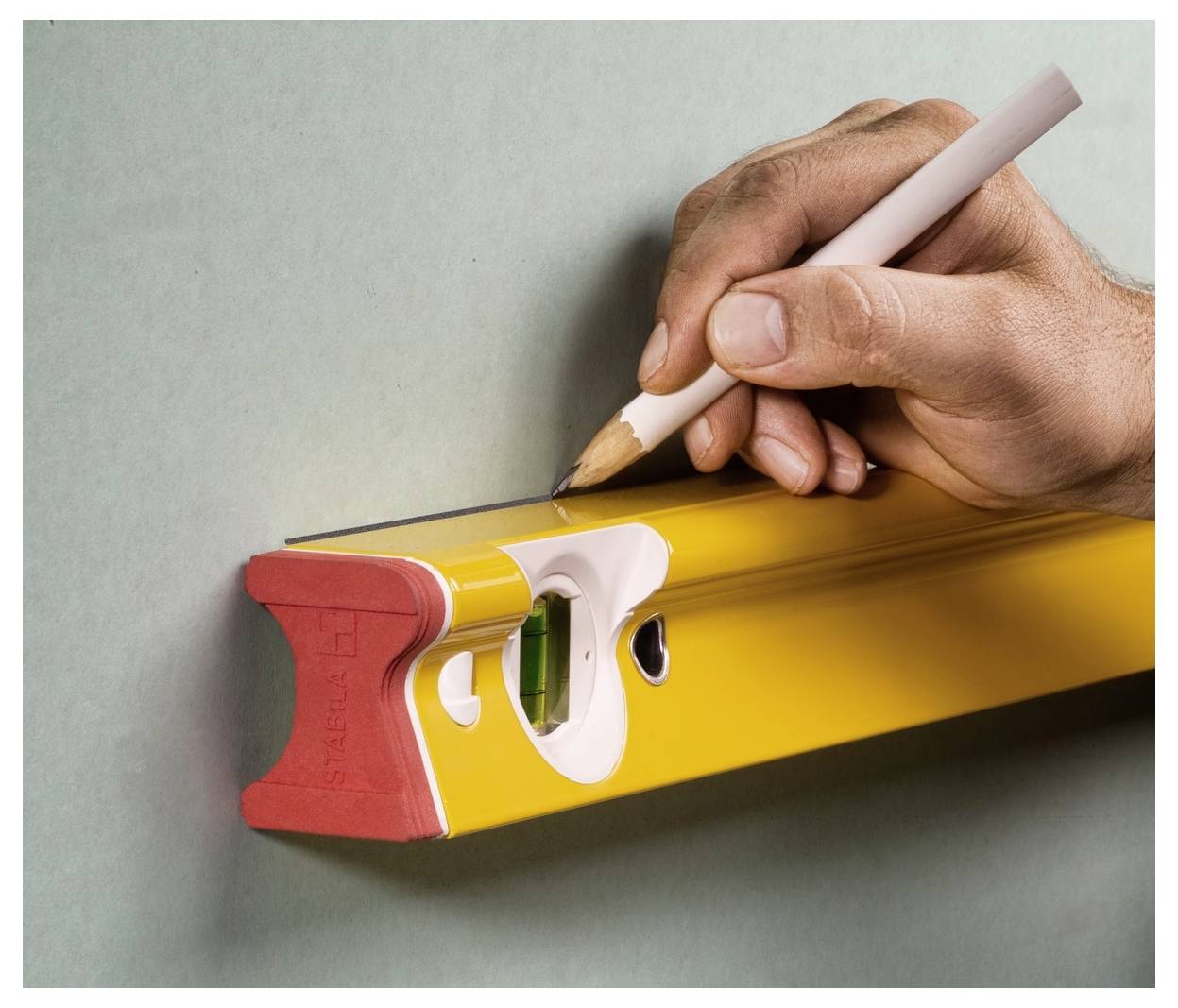 Mano che tiene una matita per segnare un livello a bolla giallo, indicando un allineamento preciso o il tracciamento di una linea retta.