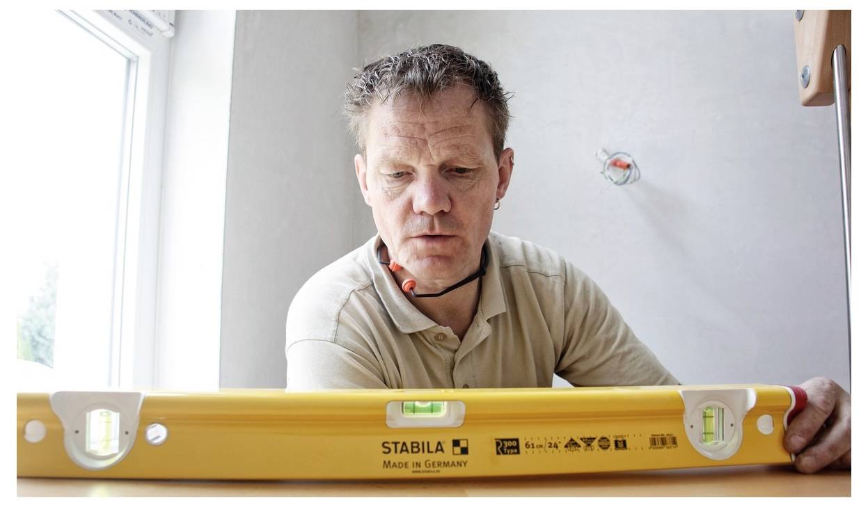 Un uomo che utilizza un livello a bolla giallo per controllare una superficie in interno vicino a una finestra.