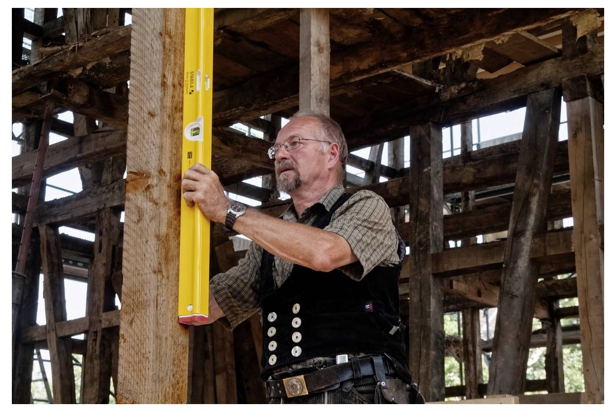 Un operaio edile che utilizza un livella a bolla gialla per controllare un palo di legno all'interno di un edificio con struttura in legno in fase di costruzione.