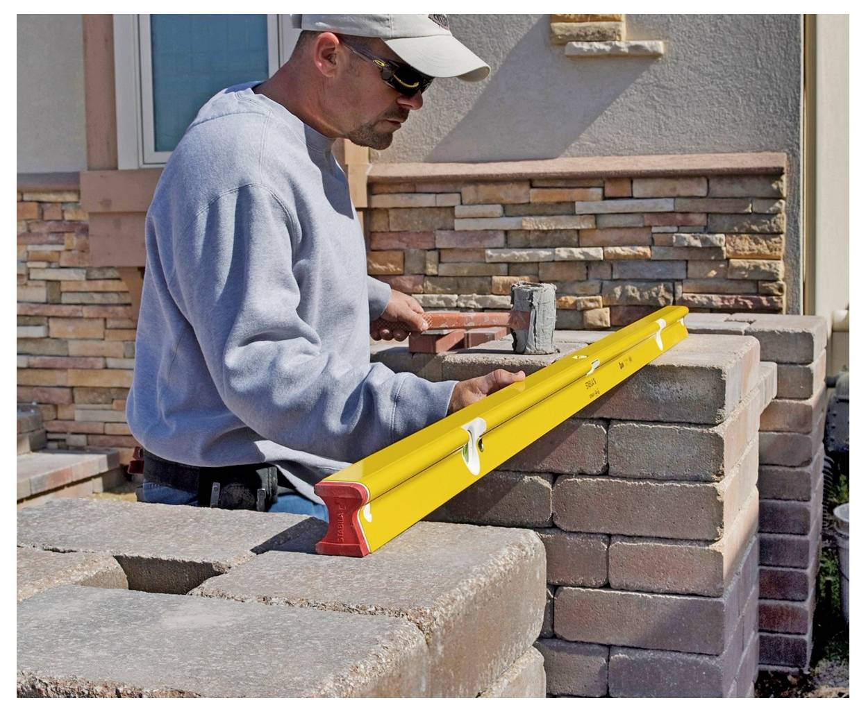 Un operaio edile sta livellando un muro in mattoni con un livello a bolla d'aria giallo brillante mentre costruisce una struttura muraria all'aperto.
