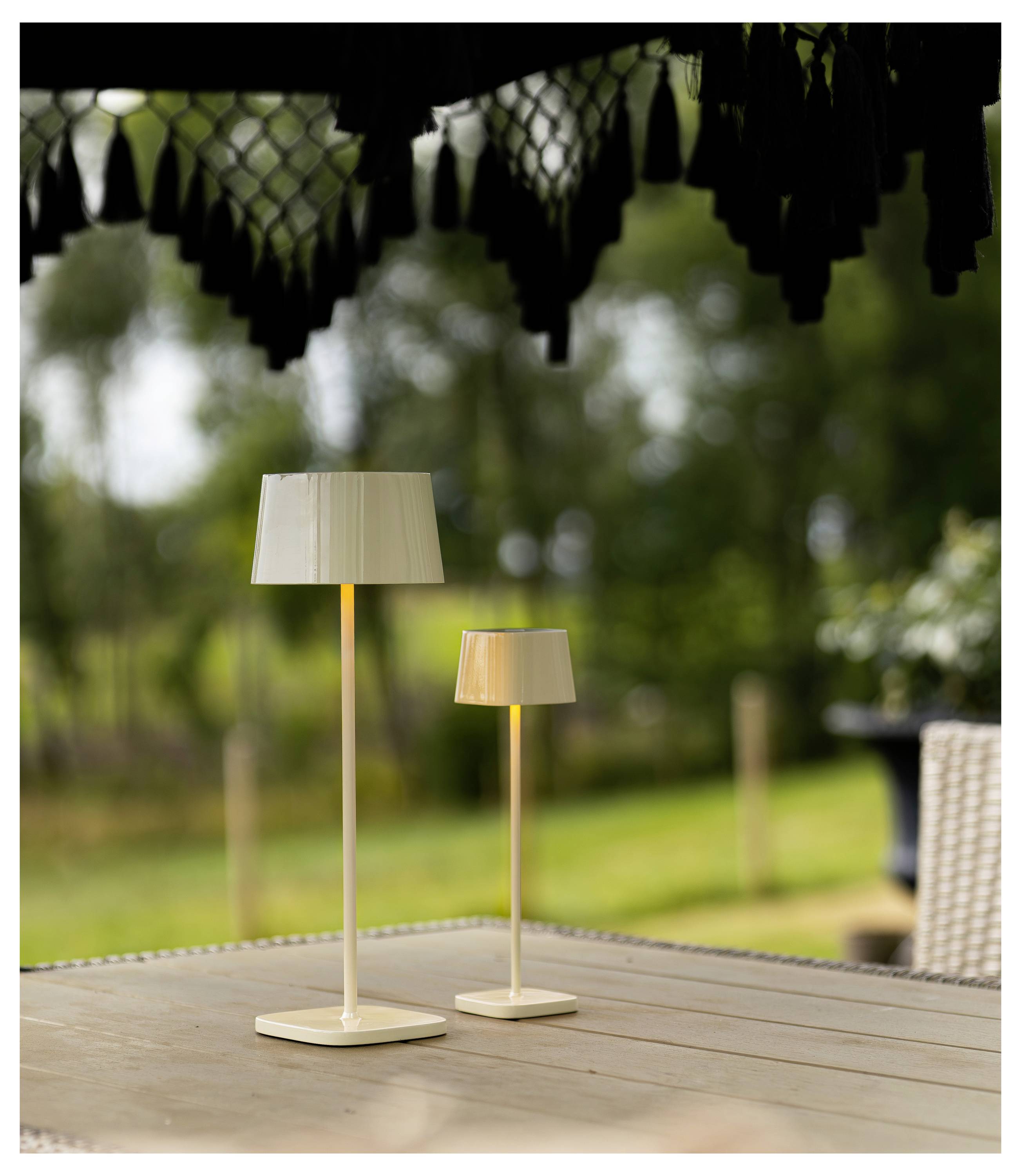 Due piccole lampade da tavolo beige con paralumi su un tavolo di legno all'aperto, con uno sfondo di giardino sfocato.