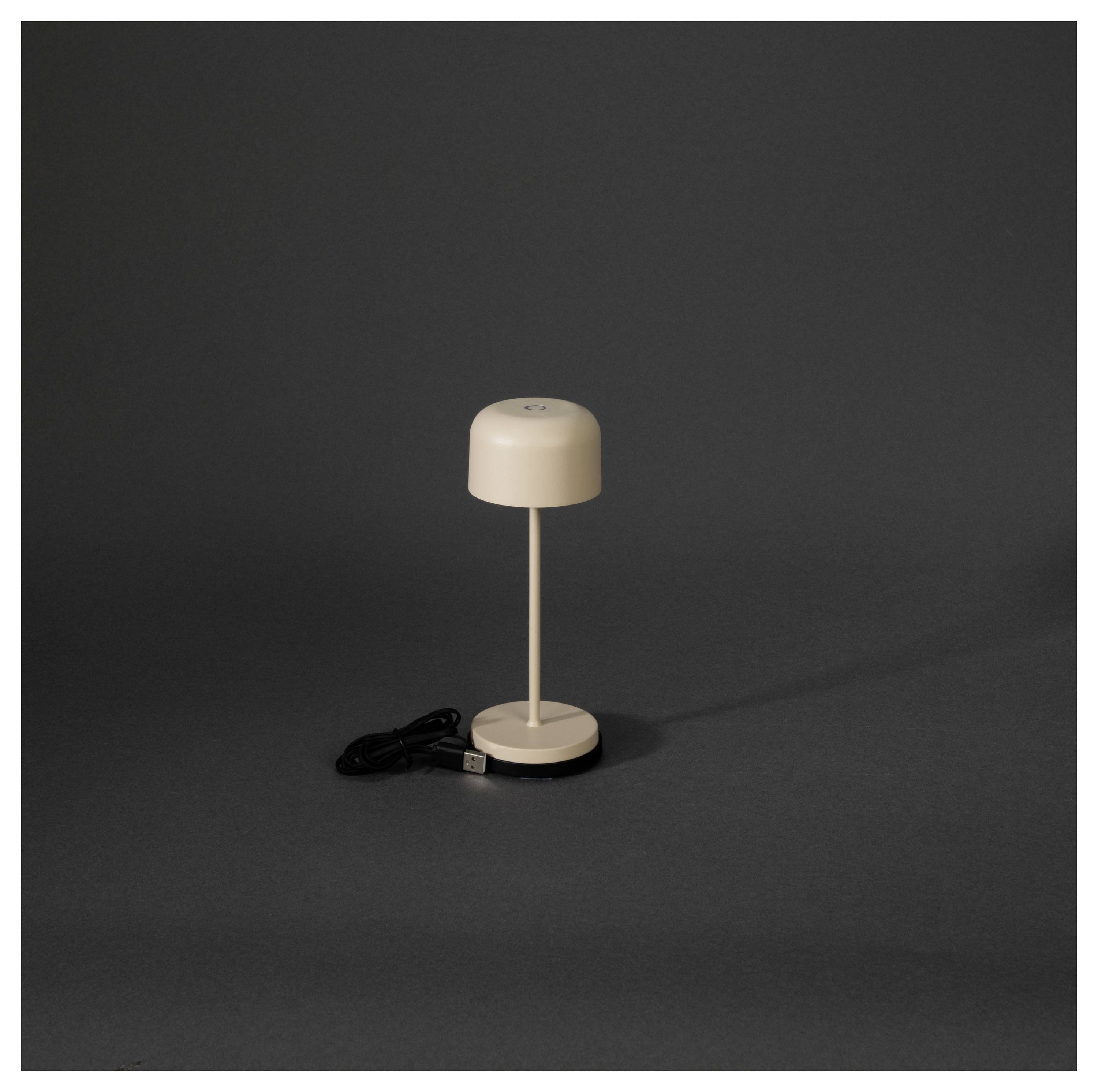 Una piccola lampada da tavolo portatile beige con un cavo di alimentazione USB si trova su uno sfondo scuro.