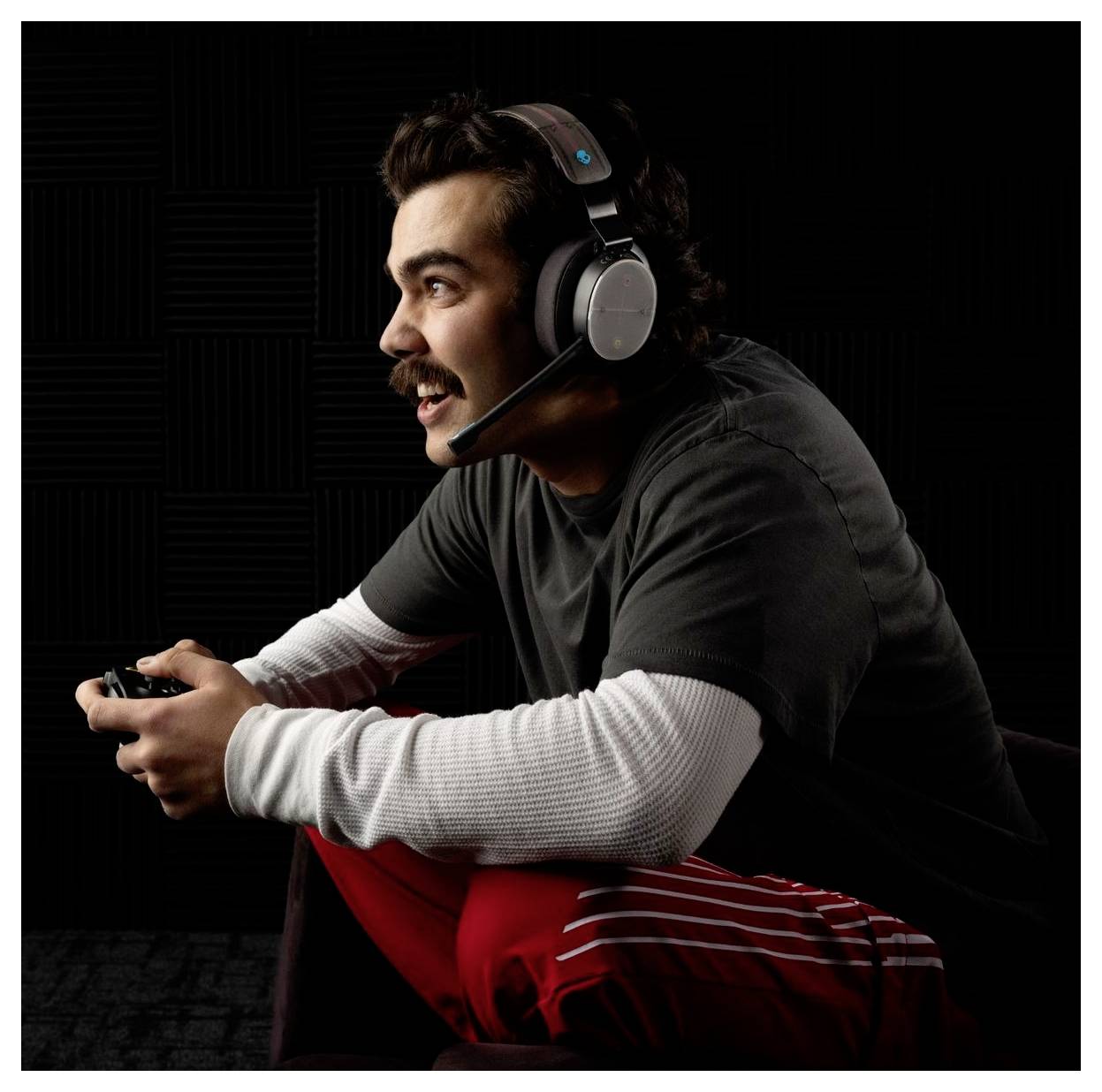 Uomo che indossa una cuffia e tiene in mano un controller per videogiochi, che si sporge in avanti con concentrazione focalizzata mentre gioca su uno sfondo scuro.