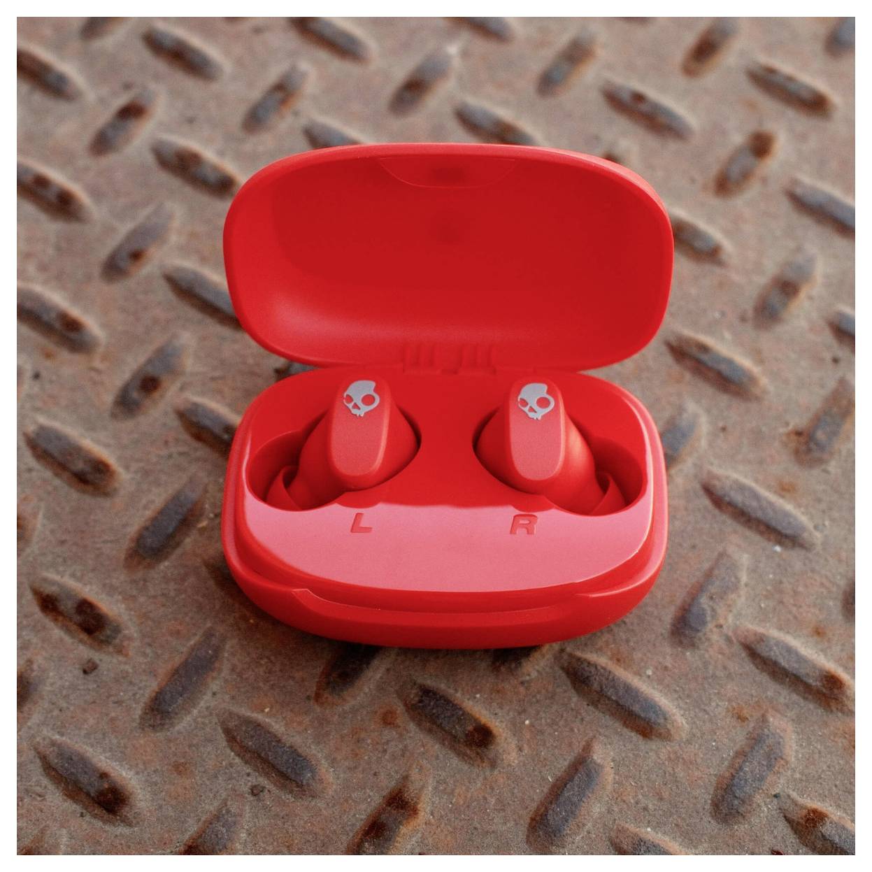 Auricolari wireless rossi in una custodia di ricarica aperta su una superficie metallica arrugginita.