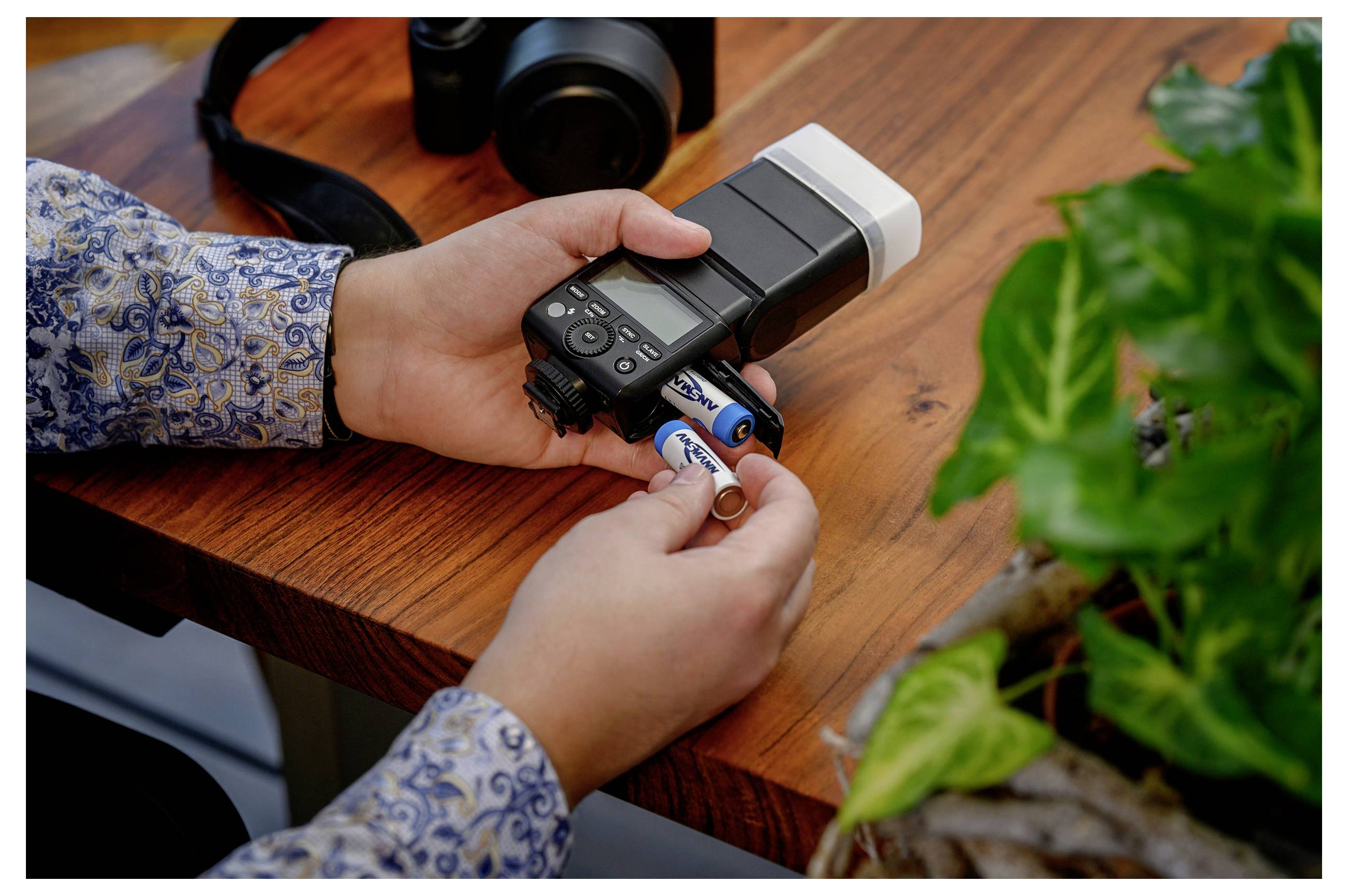 Una persona che carica batterie AA in un'unità flash fotografica su una scrivania di legno.