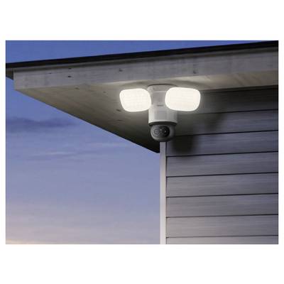 Telecamera di sicurezza esterna con due luci luminose a sensore di movimento montate sotto la gronda di una casa al crepuscolo.