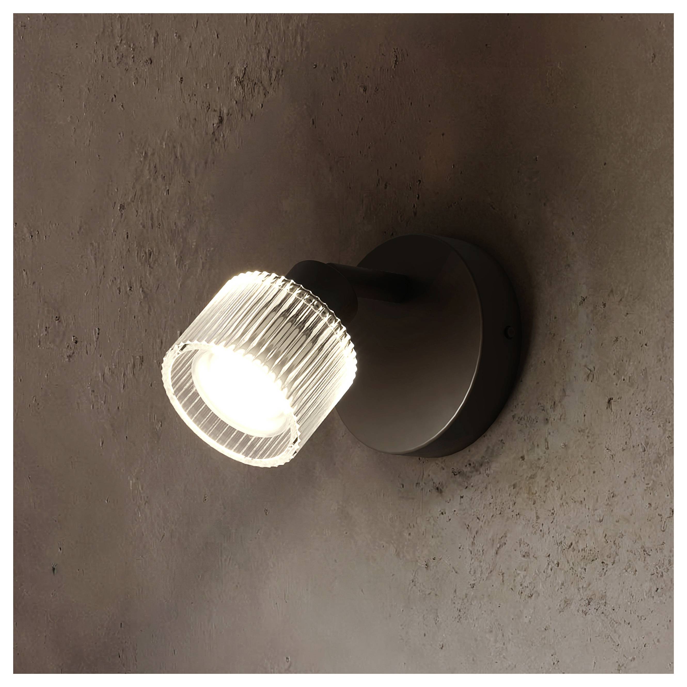 Faretto da parete con paralume in vetro rigato illuminato su una base circolare scura su un muro marrone con texture.