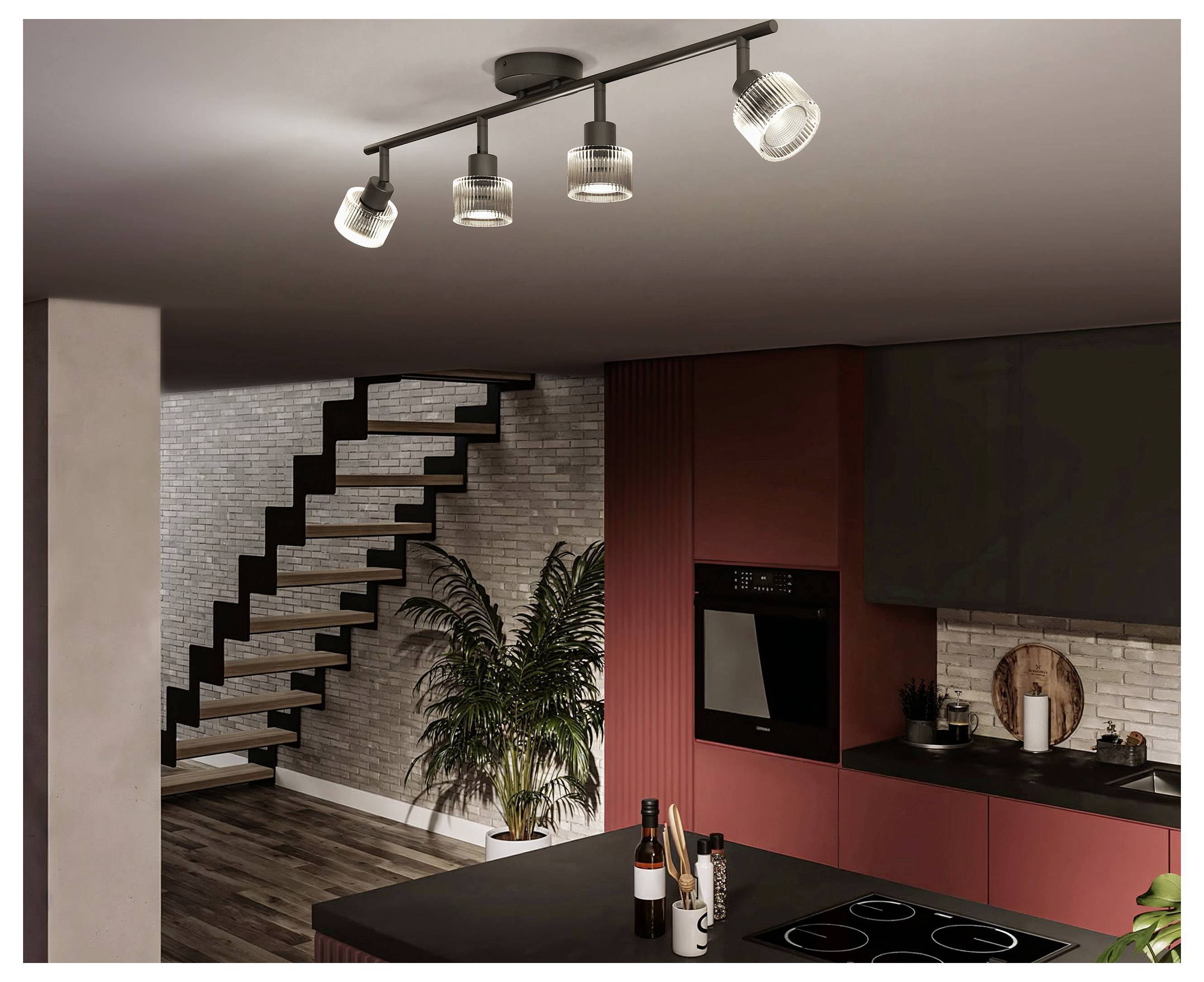 Interno cucina moderna con armadi rossi, isola nera, scala, pianta in vaso e faretti a binario sul soffitto.