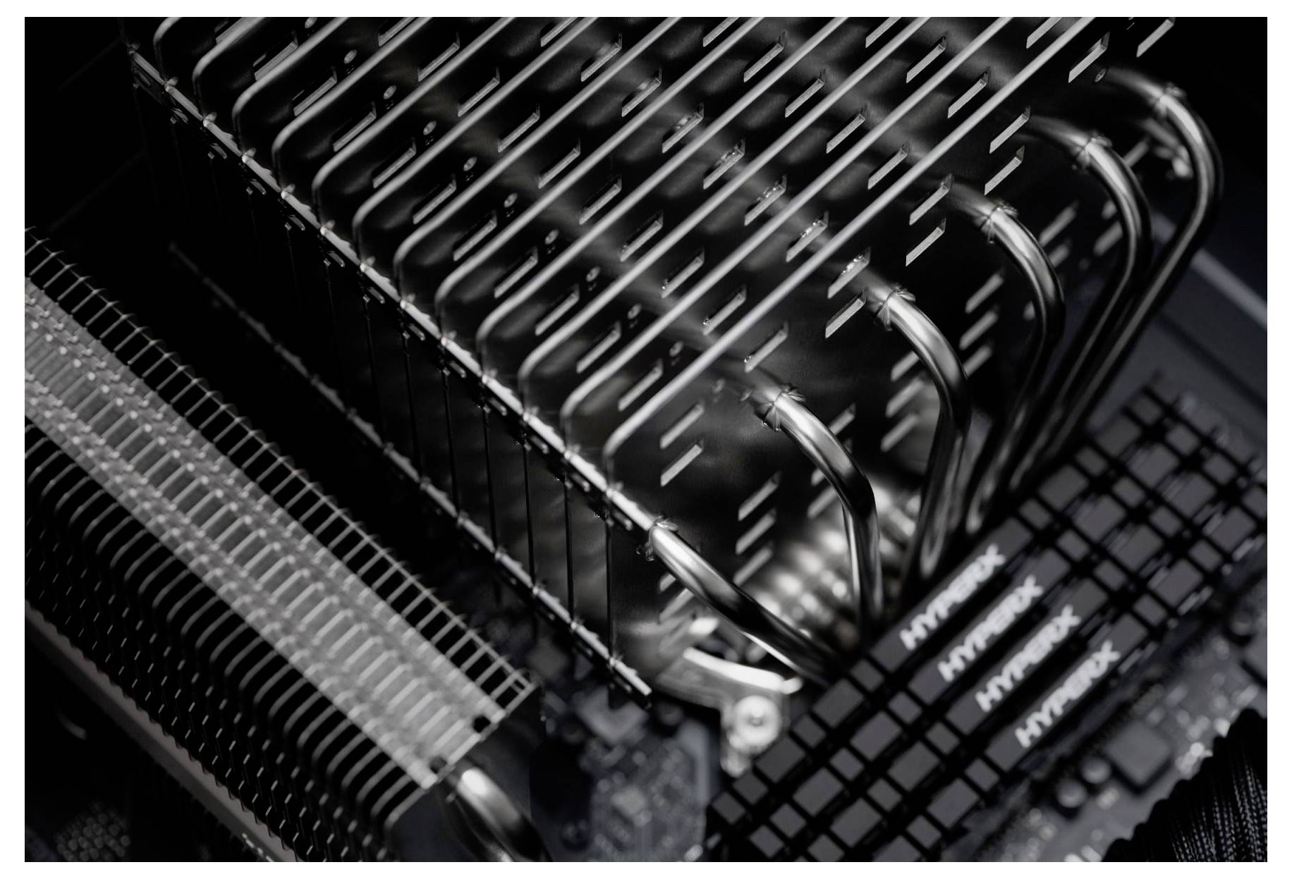 Primo piano di una scheda madre di un computer che mostra un dissipatore della CPU, tubi di calore e slot RAM all'interno di un case PC desktop.