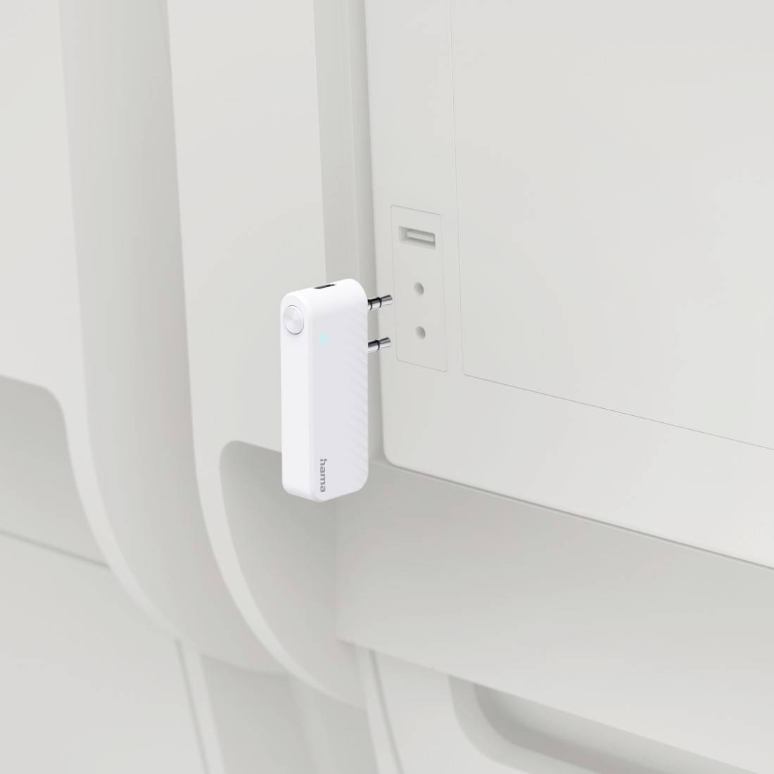 Adattatore di corrente bianco o caricabatterie inserito in una presa a muro accanto a un pannello bianco su una parete interna pulita e minimalista.