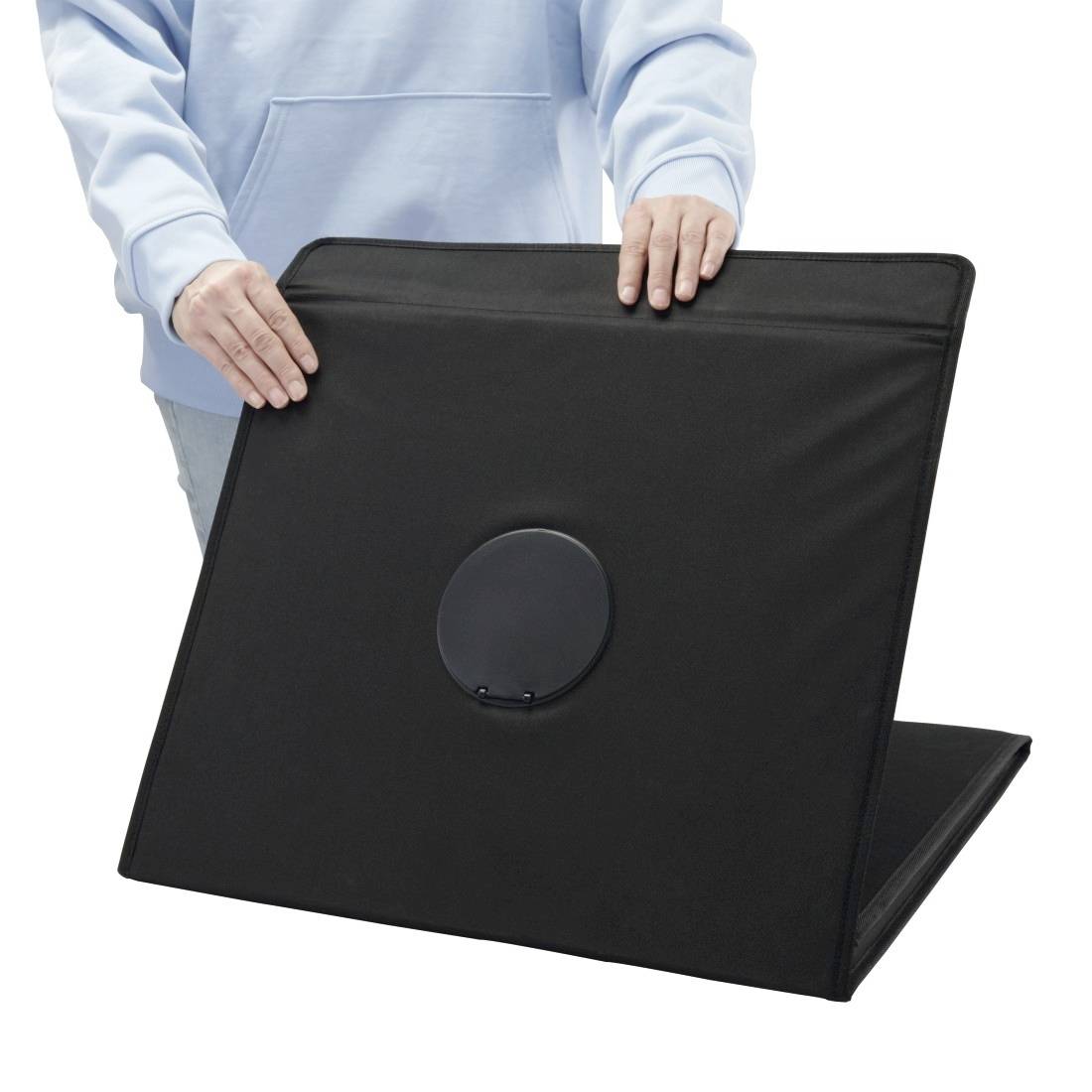Persona in una camicia blu chiaro che regge un grande pannello pieghevole nero con un'apertura circolare centrale su uno sfondo bianco.