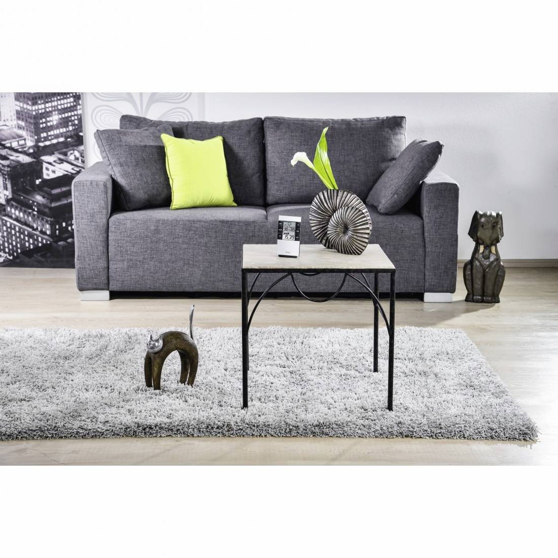 Soggiorno moderno con divano grigio, cuscino verde lime, tavolino da caffè, tappeto e sculture decorative.