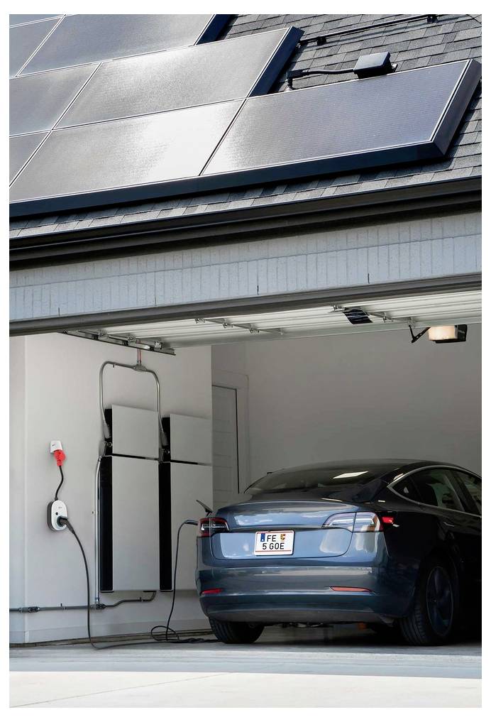 Auto elettrica parcheggiata in un garage con attrezzatura di ricarica montata a parete, sotto pannelli solari sul tetto.