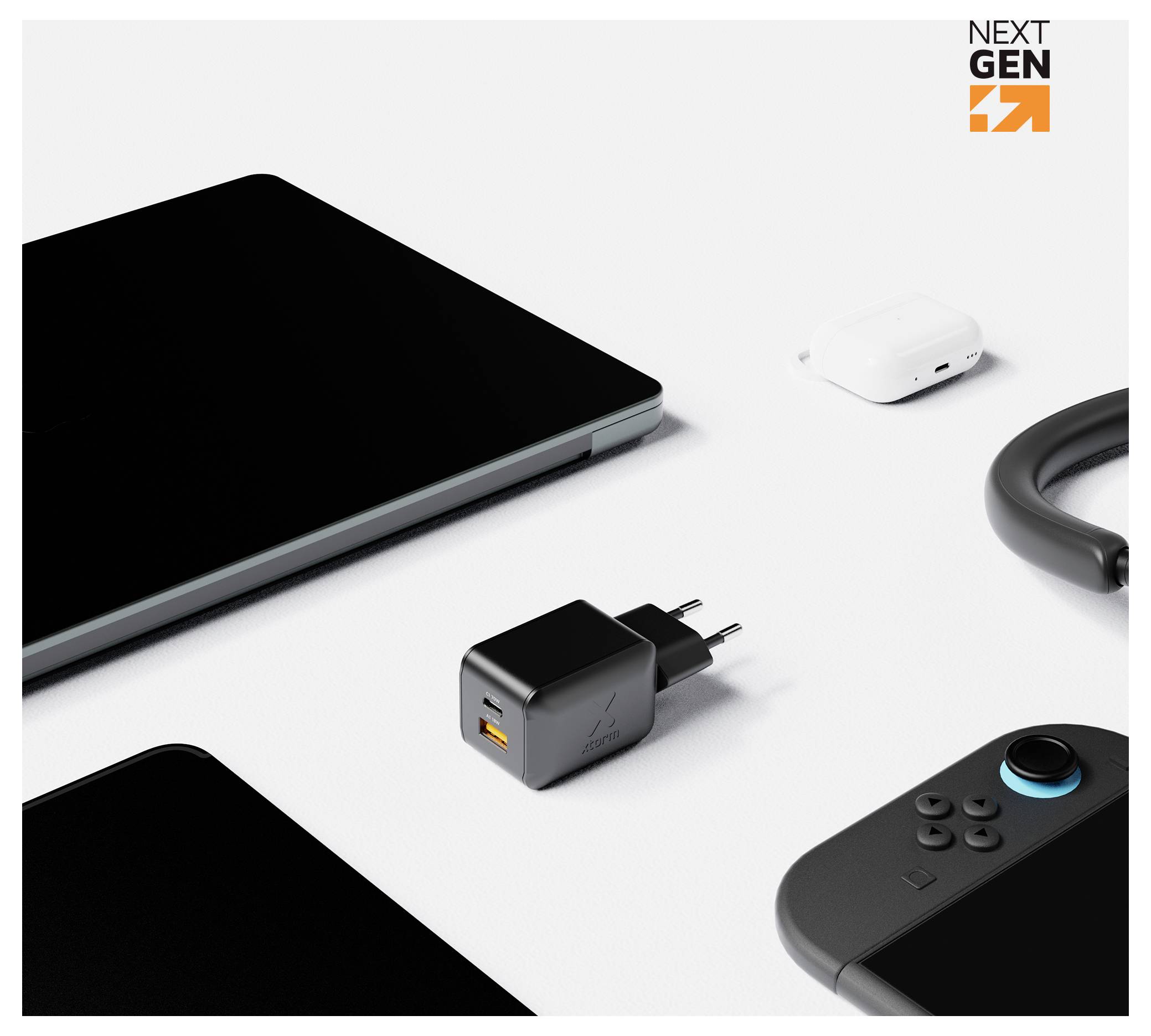 Vari dispositivi tecnologici su uno sfondo bianco, centrati su un caricabatterie USB da parete nero con porta arancione; vicino si trovano un laptop, una custodia per gli auricolari, un cavo e un controller per videogiochi.