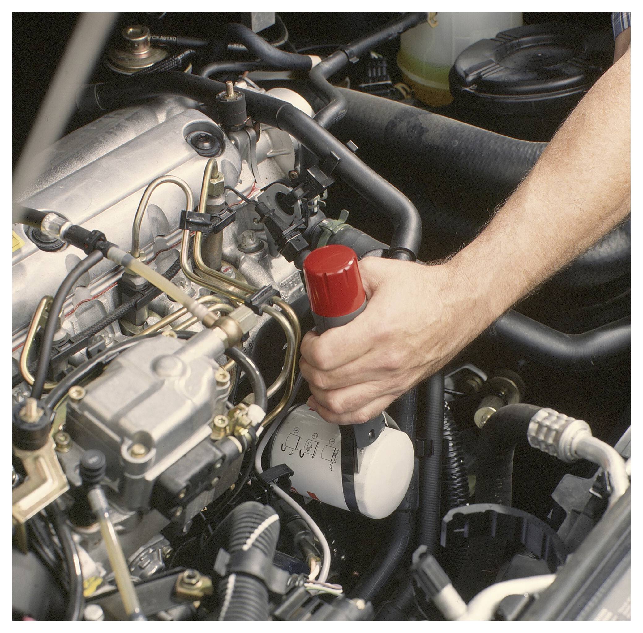 La mano di un meccanico tiene una chiave per filtri olio mentre sostituisce un filtro dell'olio motore nel vano motore di un'auto.