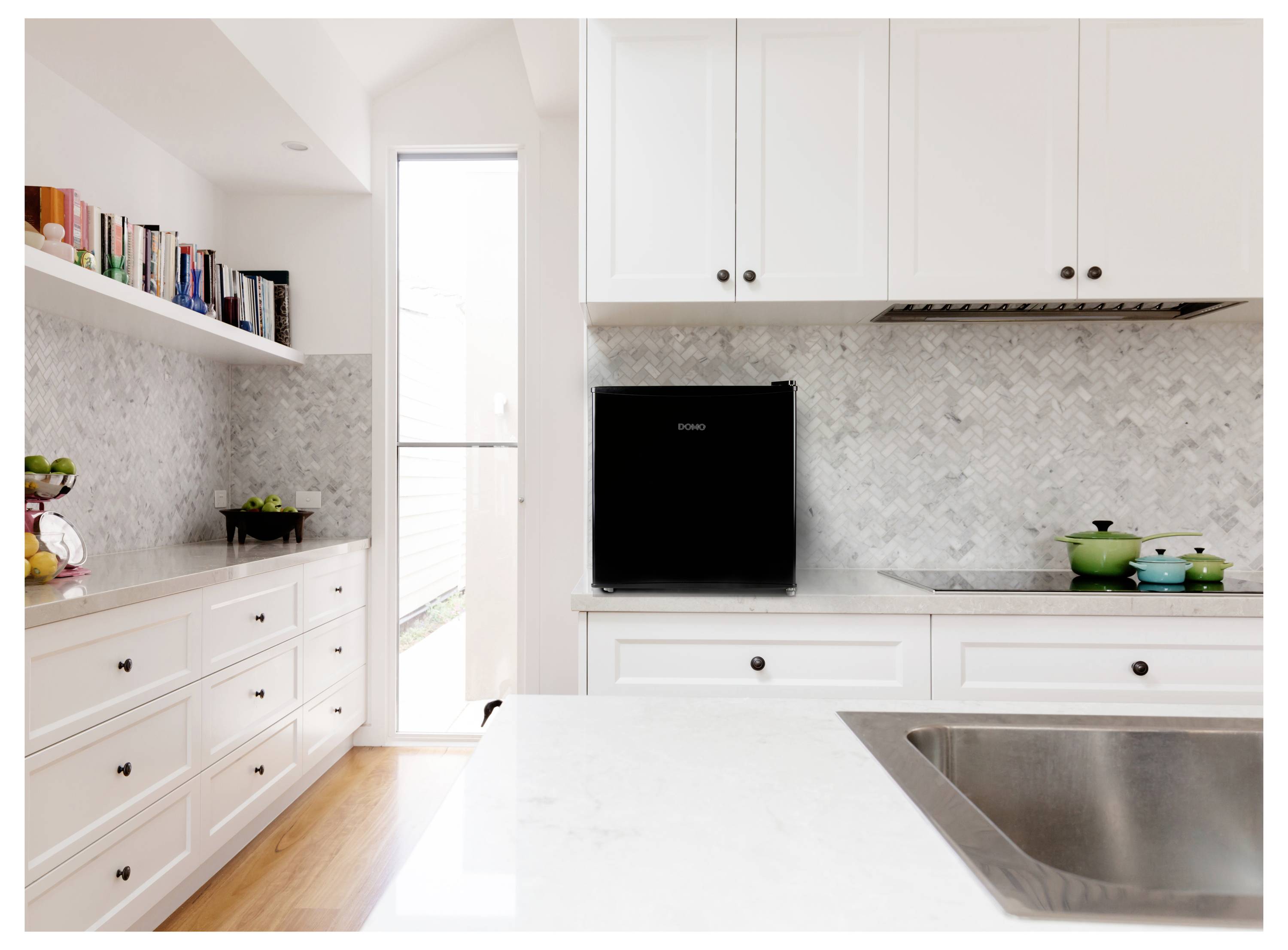 Cucina bianca moderna luminosa con armadi, scaffalature aperte, rivestimento in pietra, lavello su isola e una cappa nera sopra il piano cottura.