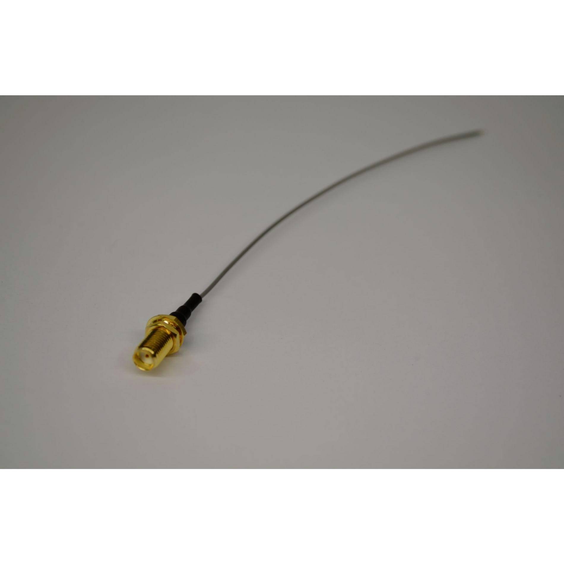 Un sottile cavo ricurvo o antenna con connettore dorato giace su una superficie bianca liscia.