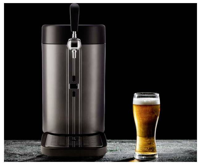 Un dispensatore di birra da bancone con rubinetto si trova accanto a un bicchiere di pinta pieno di birra ambrata su uno sfondo scuro.