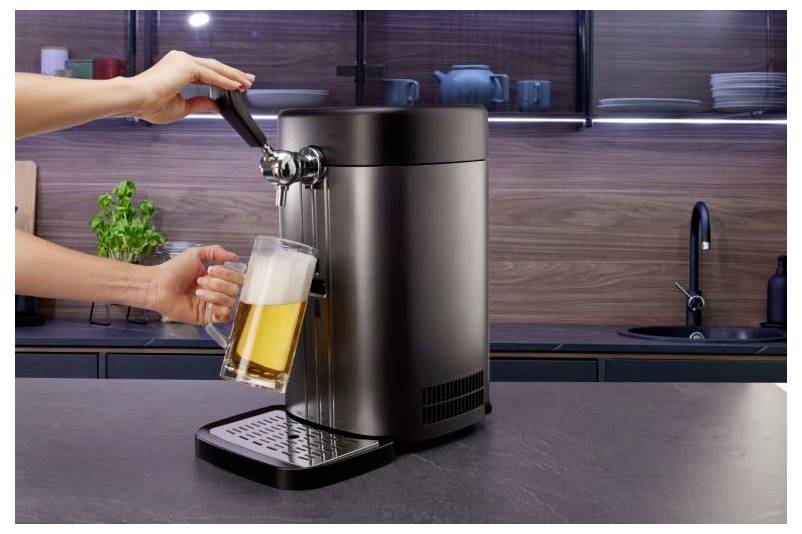 Una persona versa un bicchiere di birra da un dispenser di birra in acciaio inossidabile su un piano di cucina.