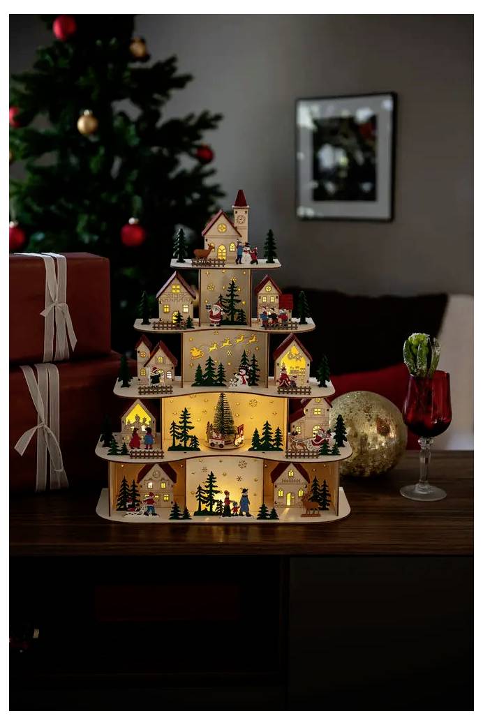 Esposizione di un villaggio natalizio in miniatura illuminato a forma di albero su un tavolo accanto a regali incartati e un albero decorato.