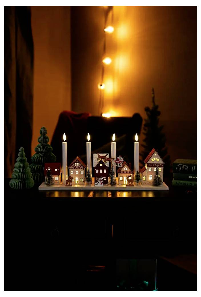 Esposizione di un villaggio natalizio in miniatura con candele accese e piccole case su un tavolo, sullo sfondo di luci decorative calde e luminose.