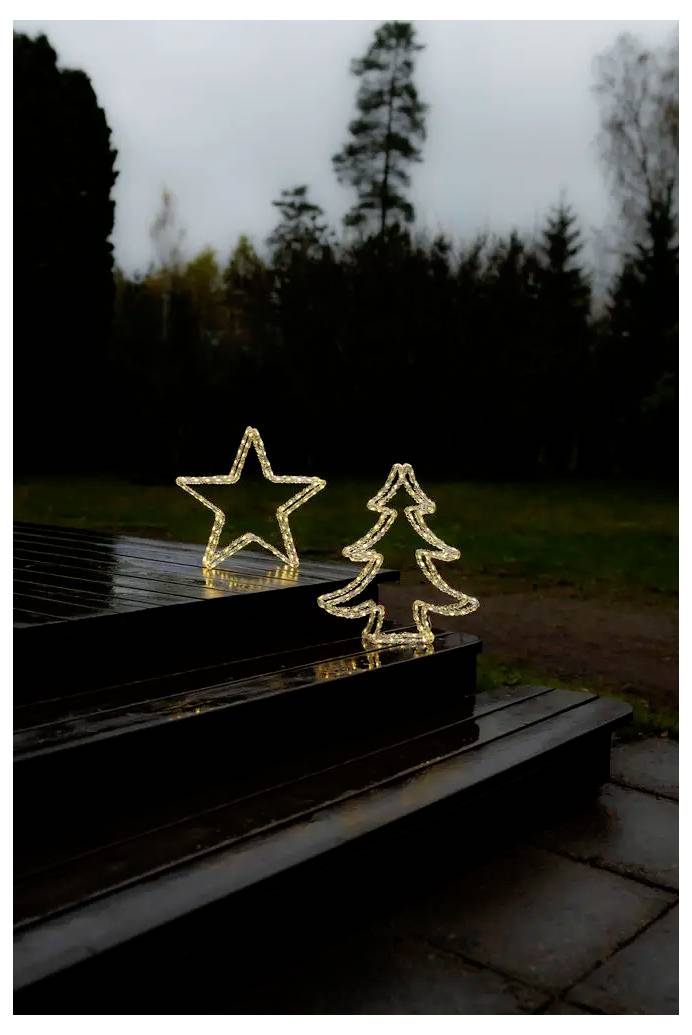 Decorazioni natalizie illuminate con stella e albero di Natale su scale esterne buie in un parco al tramonto.