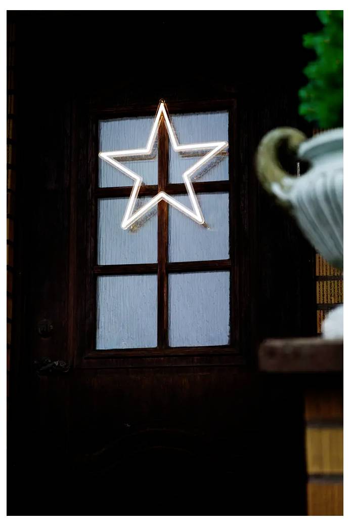 Una luce a forma di stella luminosa appesa nella finestra di una porta di legno scuro, con una pianta o un vaso sfocato in primo piano.