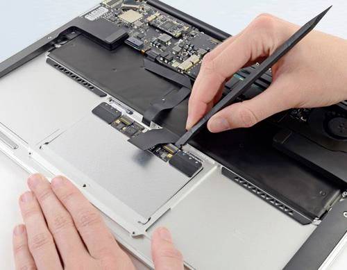 Mani che utilizzano pinzette per scollegare un cavo all'interno di un laptop aperto durante la riparazione.