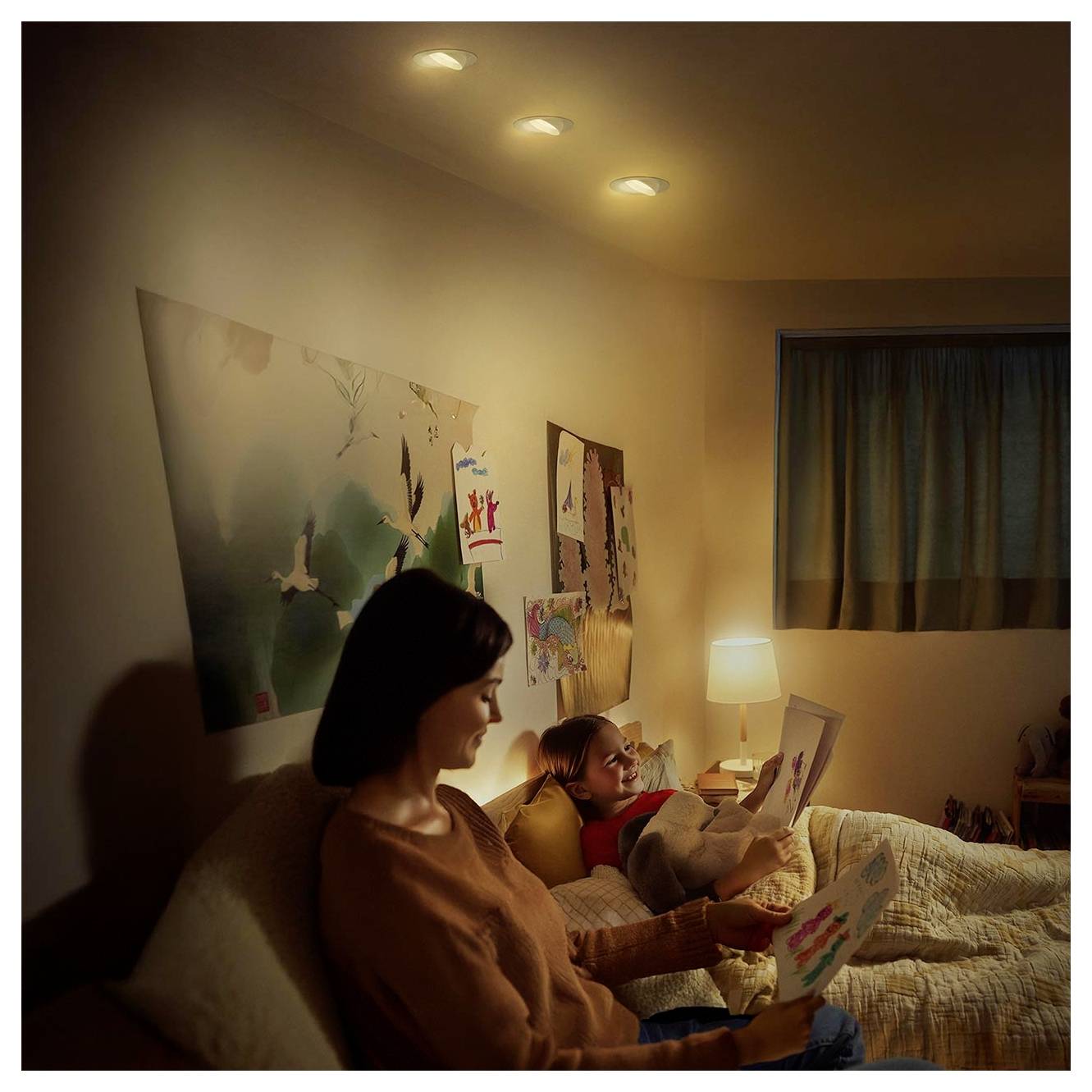 Donna e bambino seduti in una camera da letto buia, che leggono libri insieme alla luce di una lampada da comodino di notte.