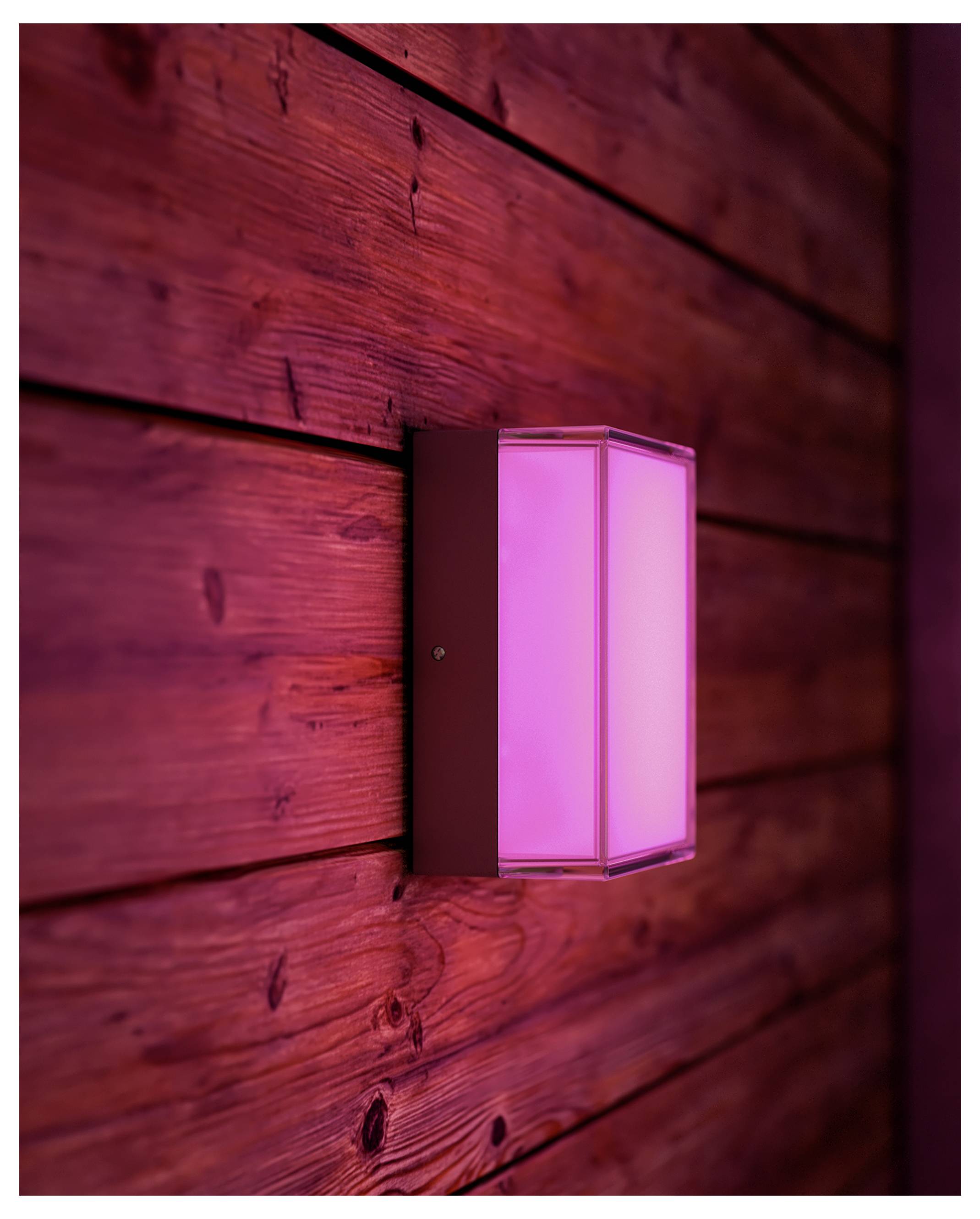 Applique da parete illuminata di rosa su una parete in assi di legno, che proietta una luminosità magenta in uno spazio interno poco illuminato.