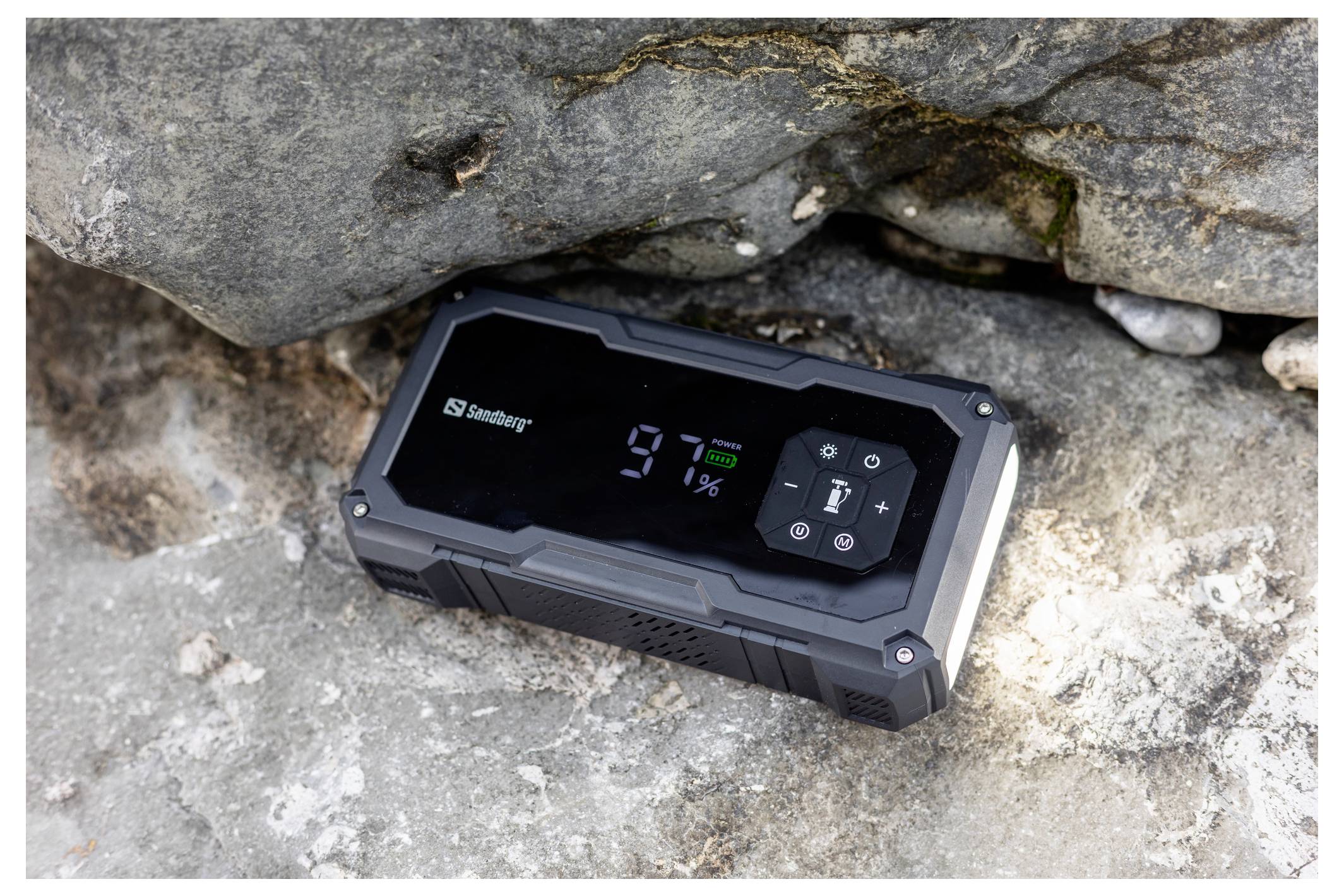 Robusto power bank portatile nero appoggiato su rocce, il suo display mostra il 9% di batteria rimanente.